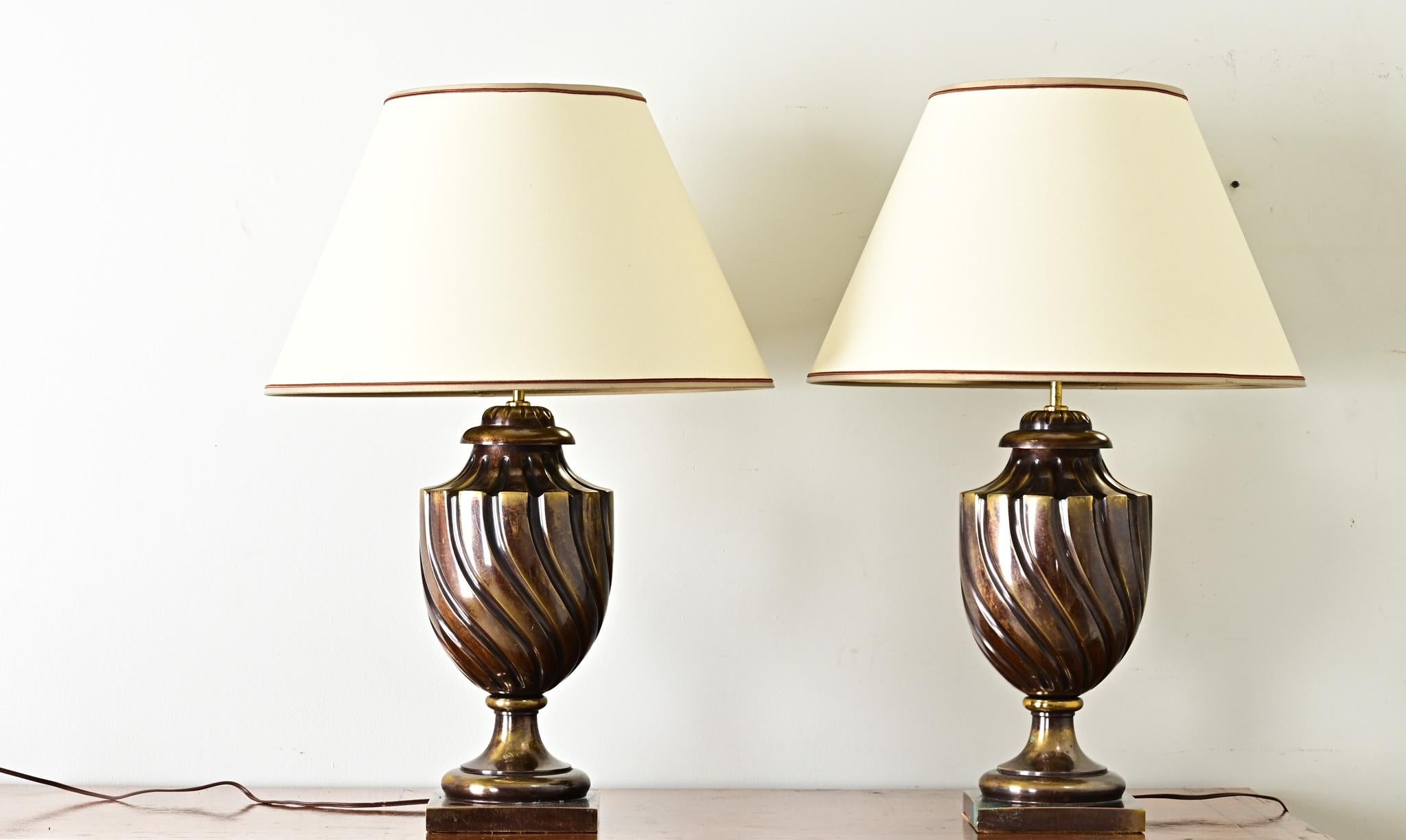 Exceptional pair of vintage brass table lamps in the style of Frederick Cooper and Stiffel, these footed urn bases have surprising weight behind their twisting design. The brass trophy form is wonderfully patinated to dark bronze with dappled