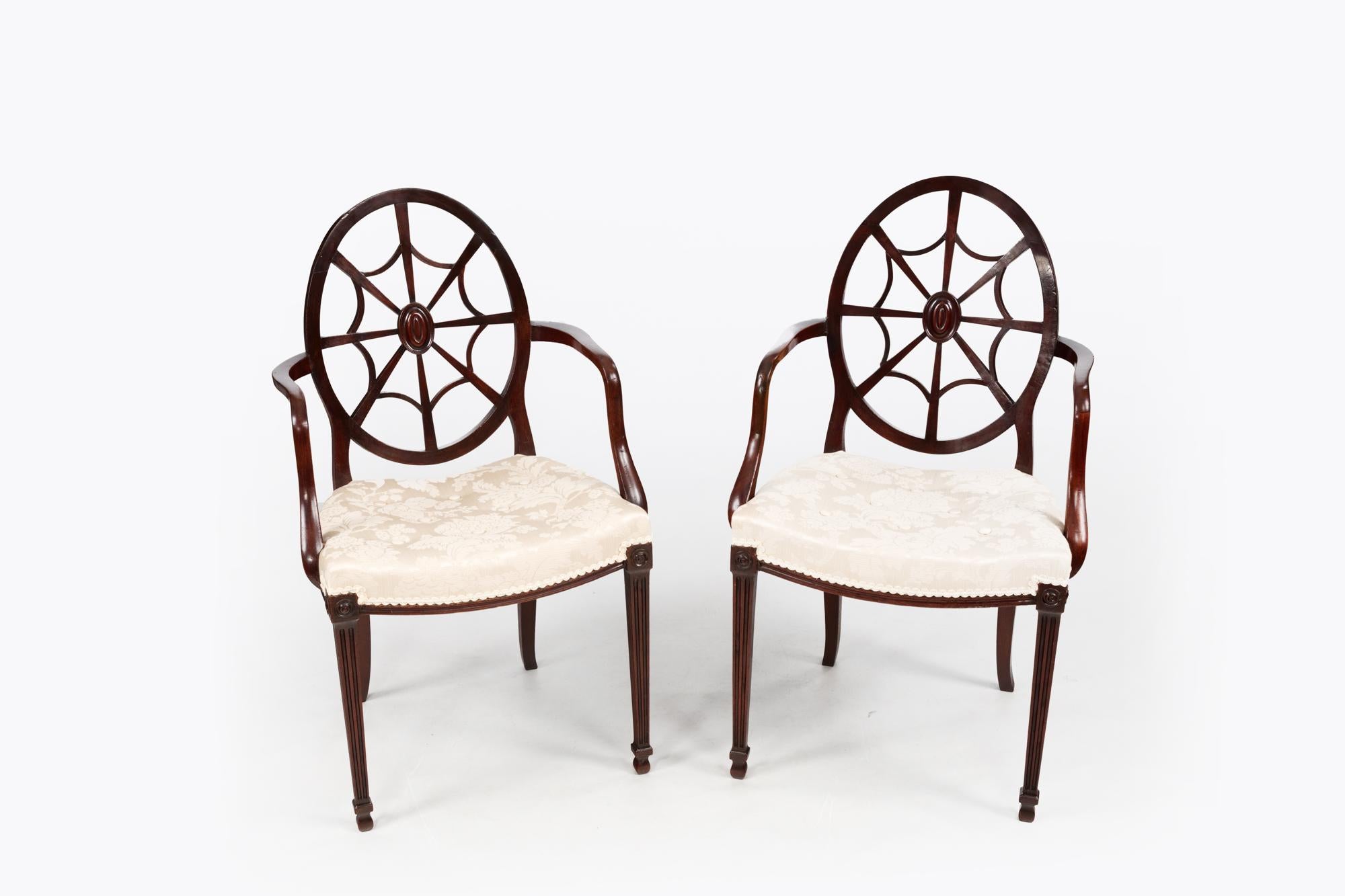 A fine pair of Hepplewhite style wheelback armchairs with oval-shaped backrests and spiderweb detailing, shaped reeded armrests & stuffed over seats. These chairs are raised on tapered spade front legs and sabre back legs. Circa early 19th century.