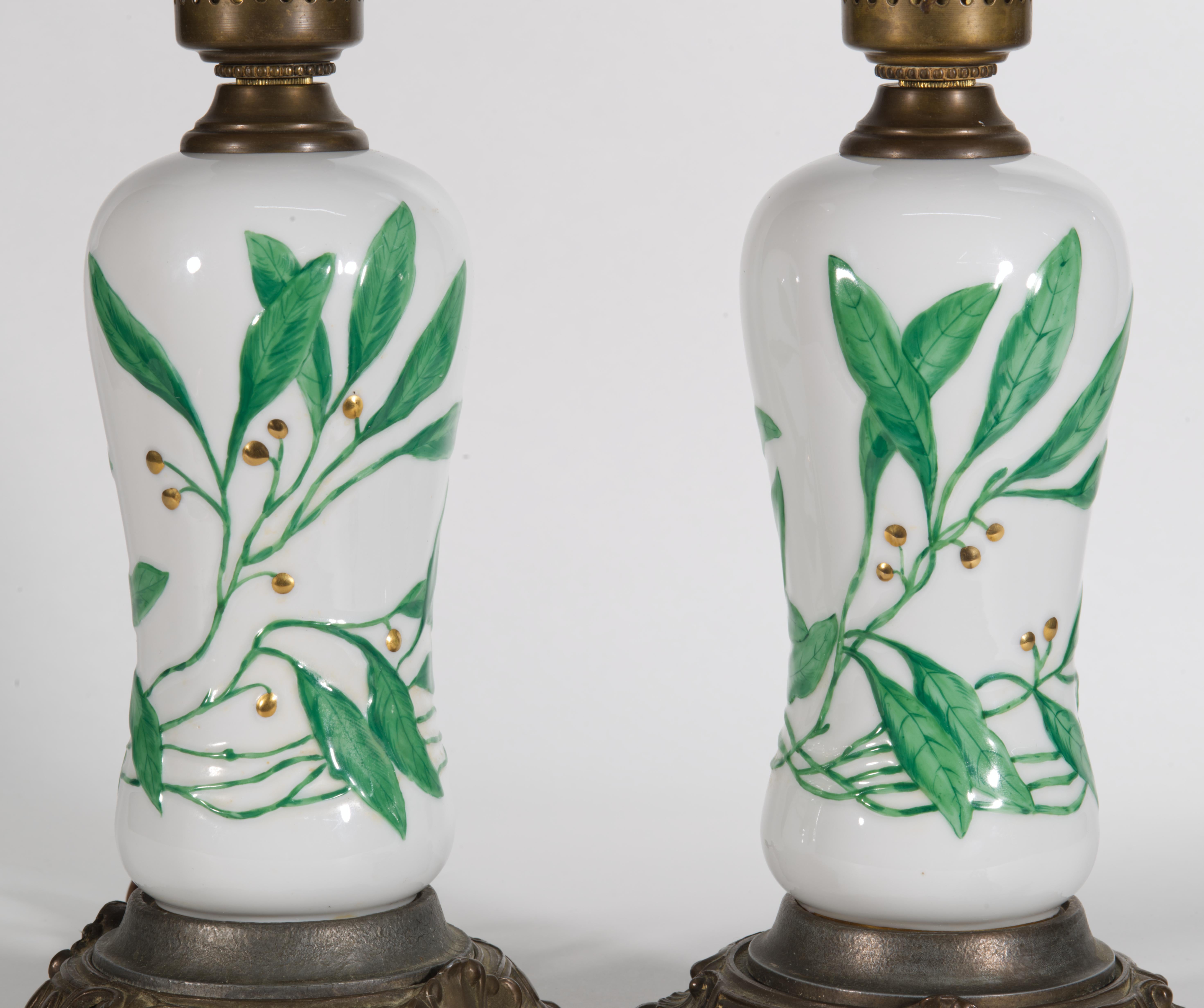 Rare, unusual pair of table lamps feature elongated porcelain bodies, mounted on ornate patinated bases and topped with matching original fittings. The elegant Art Deco style decor is done in relief and then hand-painted over with motifs of leaves