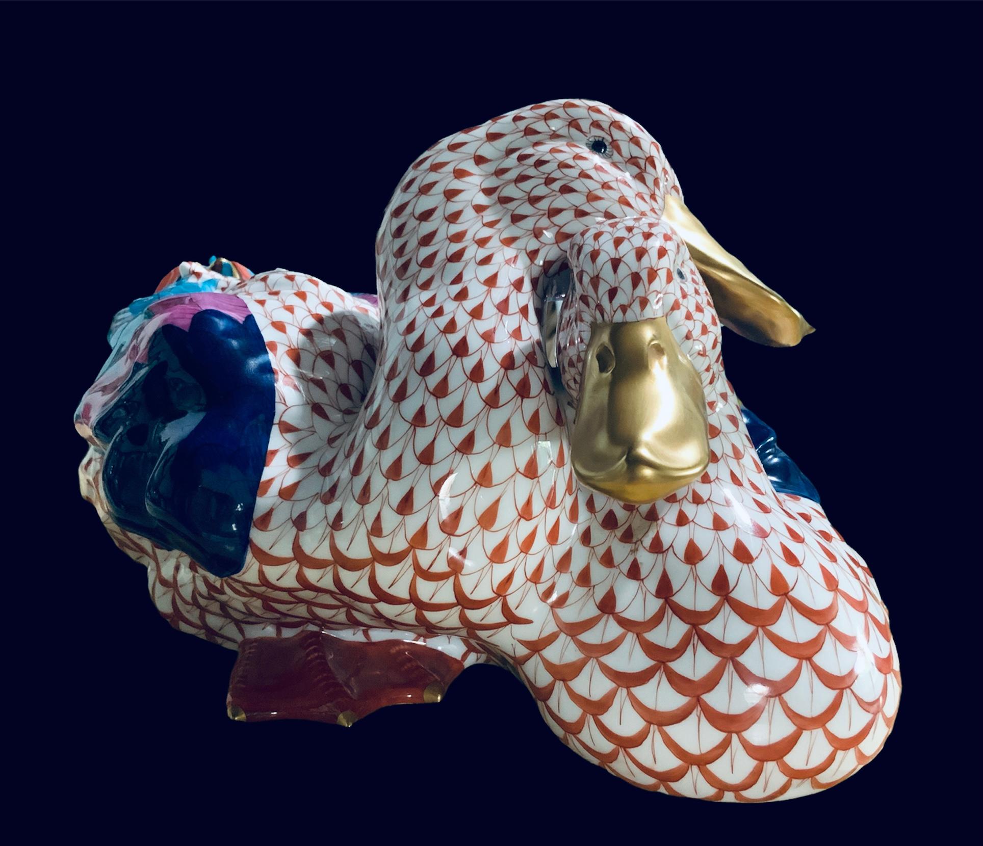 Il s'agit d'une paire de canards de grande taille en porcelaine Herend, peints à la main. Leur fond est blanc avec un motif de filet en écailles de poisson orange. Leurs ailes sont peintes à la main en bleu marine, rose et turquoise. Les plumes de