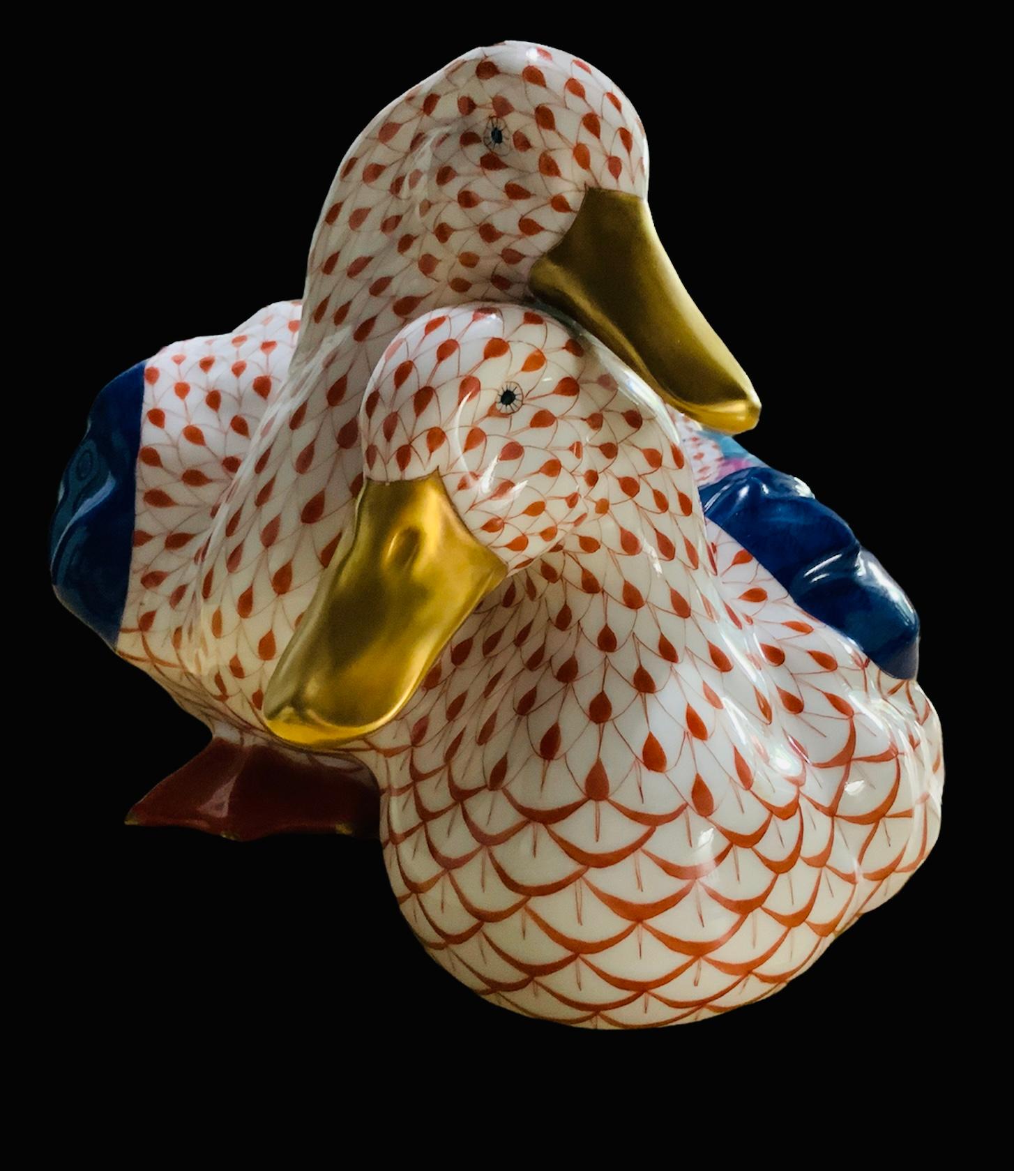 This is a pair of Herend porcelain hand painted medium size ducks. Their background is white with orange fish scale net pattern. Their wings are hand painted navy blue, pink, and turquoise color. Their tail feathers are orange, gold, turquoise, and
