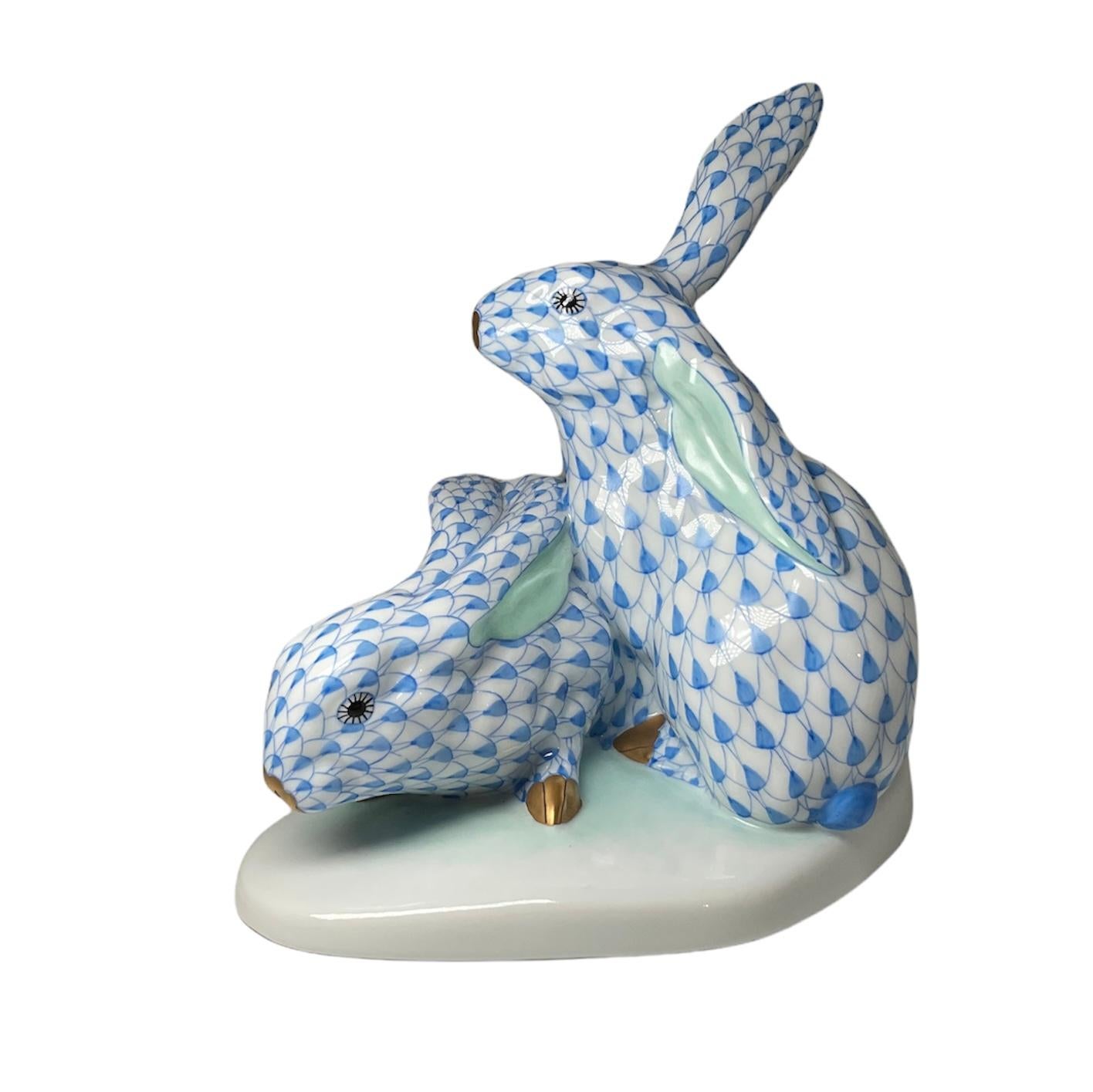 This is a pair of Herend porcelain hand painted rabbits. Their background is white with royal blue fish scale pattern. The inside of their ears are green. Their eyes are black. Their muzzles and feet are gilded. They are standing over an