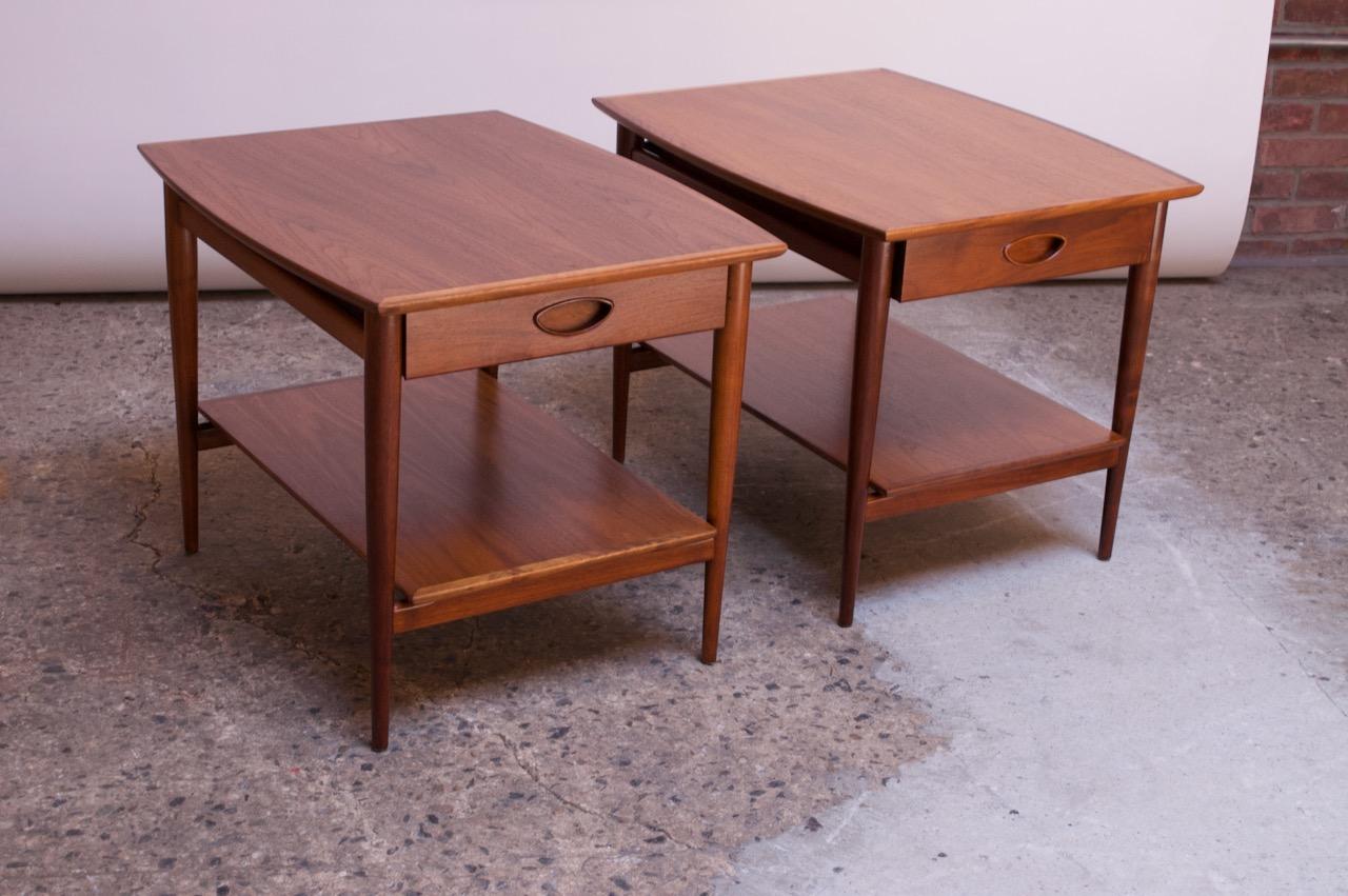 Pair of 1950s Heritage-Henredon walnut nightstands / side tables. Composed of two tiers for surface space along with a single drawer finished with a deeply sculpted, recessed pull.
Newly refinished condition; minor wear remains.
Interior drawer is
