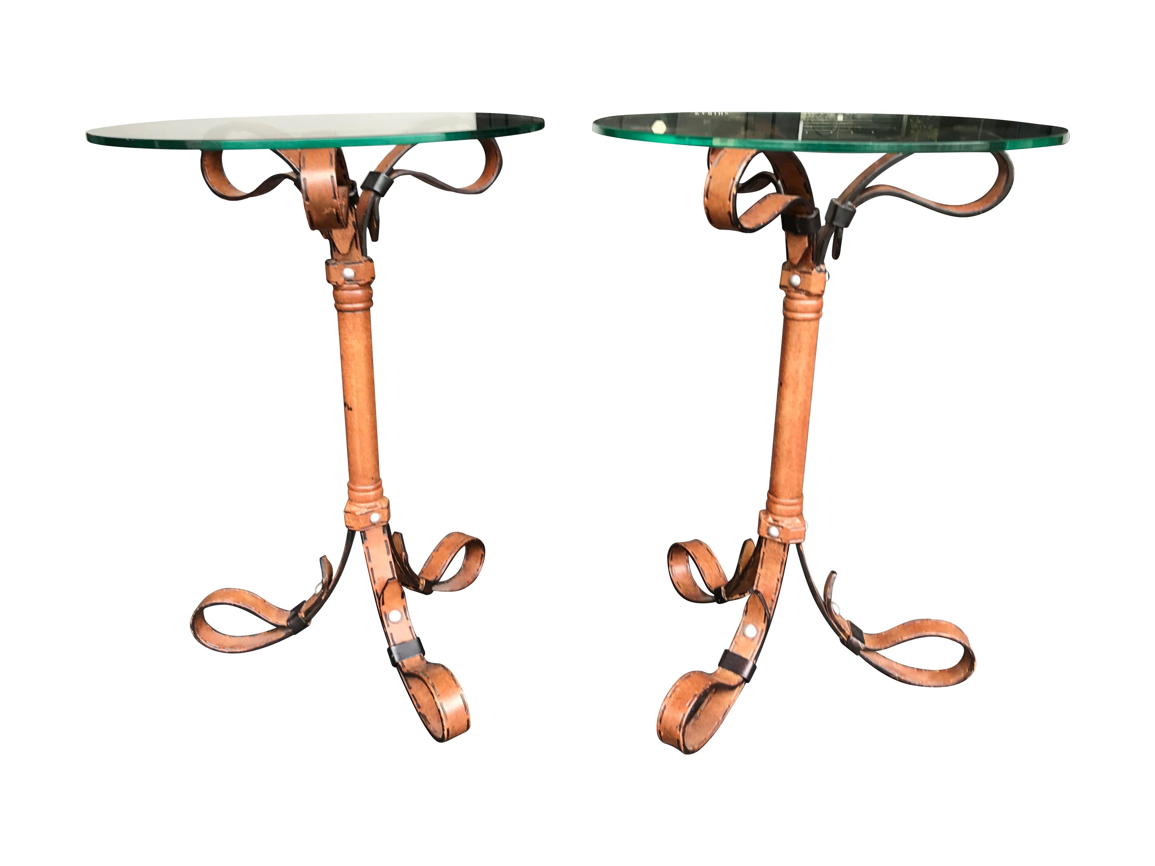 A pair of Hermes style strap side tables with metal frame with faux leather buckles and stitching with circular glass tops.