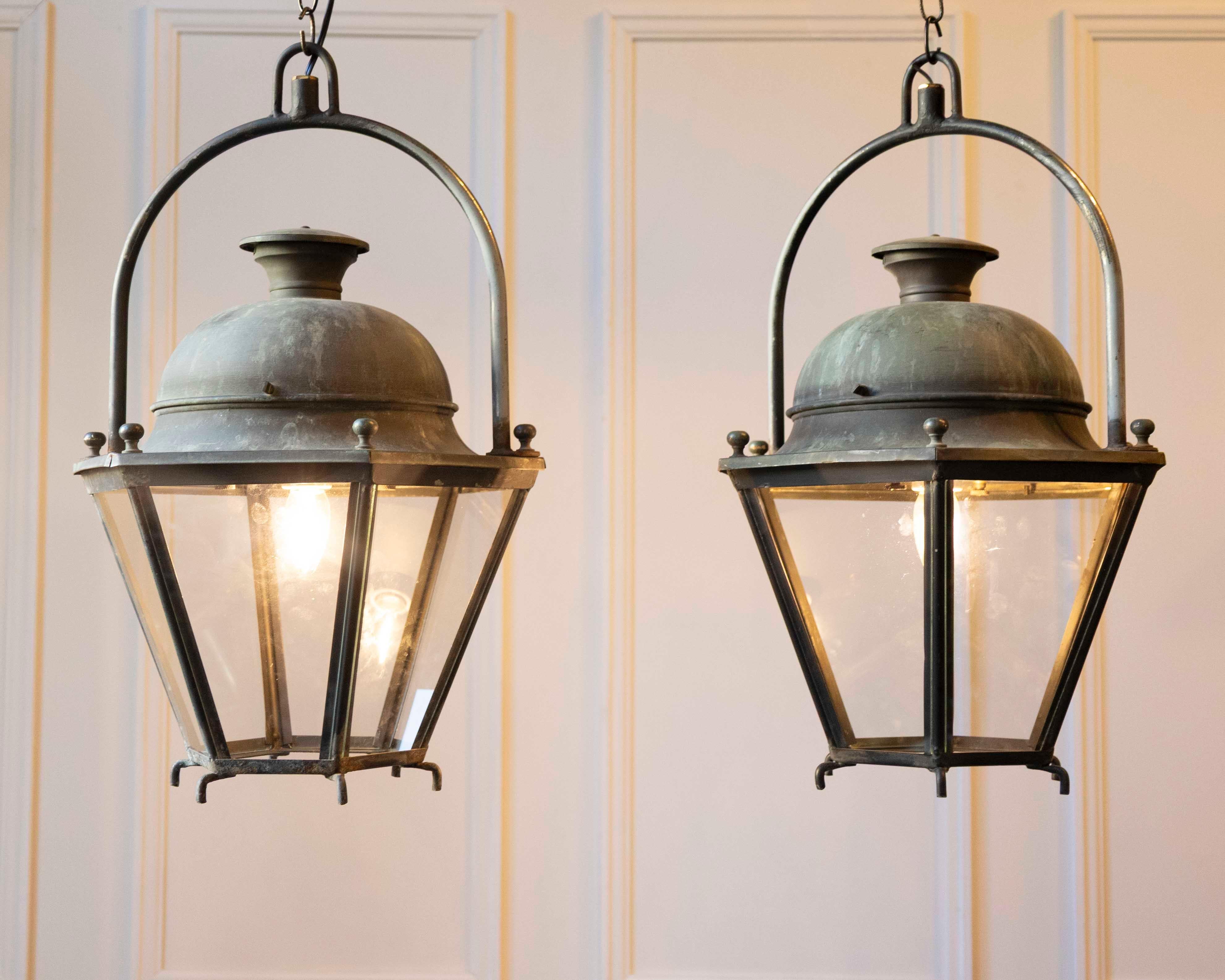 
This pair of French hexagonal copper lanterns from the 20th century reflects solid craftsmanship and restrained, traditional design. Each lantern features clear glass panels set within a copper frame, topped by a simple domed cap. The metal shows a