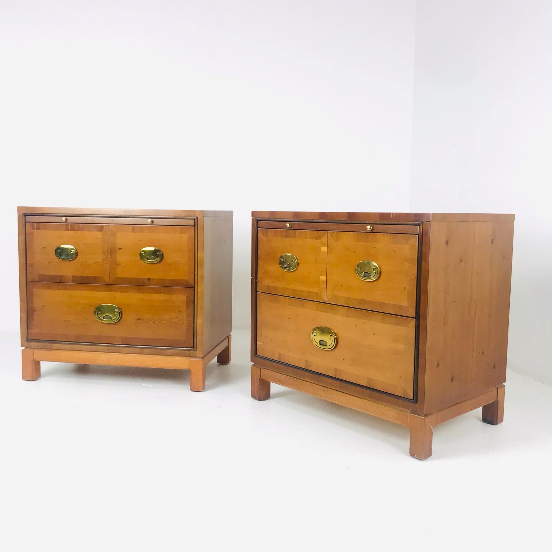 Pair of Hickory campaign style nightstands or three-drawer chests beautifully crafted with a clean modern form. Featuring a pull-out tray, stylized campaign hardware and a Ming style base. Signed Hickory Manufacturing Co. in a drawer.