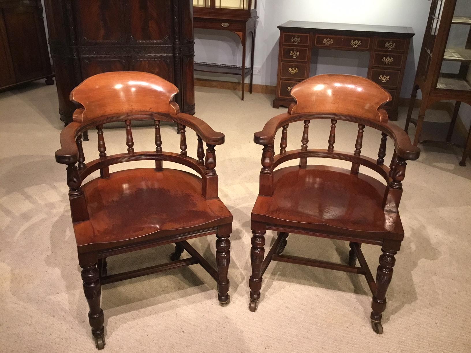A pair of high quality mahogany late Victorian period desk armchairs. Each chair having a curved solid mahogany back support with open arms and turned spindle supports. Having generous solid mahogany dished saddle seats. Supported on ring turned