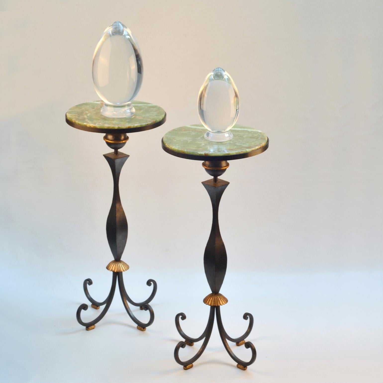 A pair of wrought black lacquered and gilt iron pedestal tables housing trays of green onyx plates. The central legs are swelled at the lower part support in the shape of a gold ringed ball on a four spiral scrolled legs. The legs rest on small