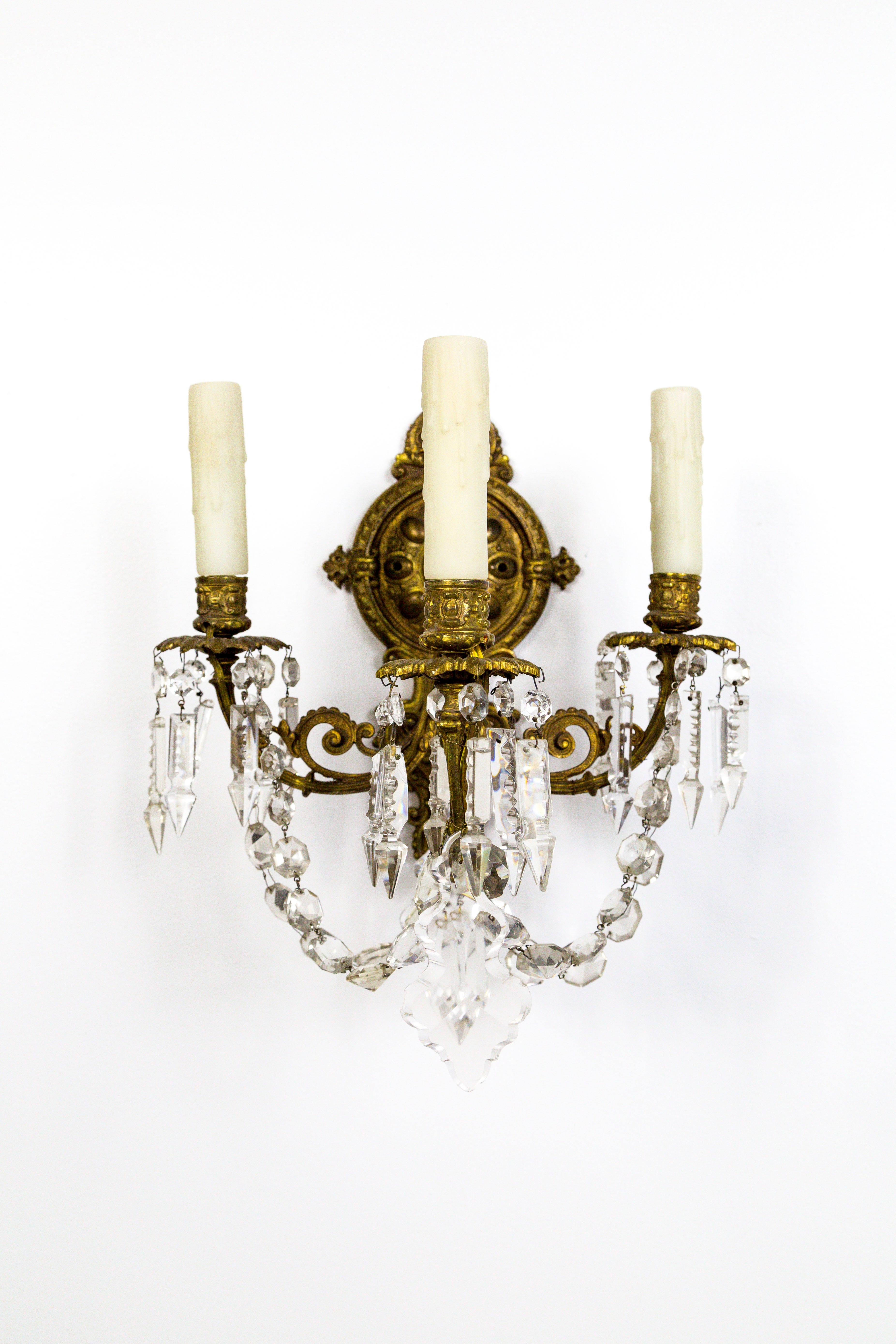 A striking pair of elaborate, French sconces in the Belle Epoque style. The detailed, solid brass structure is extra deep, with low swooping, rope crystals that echo the scroll shapes that come together at a midpoint with a crystal spear. Dressed