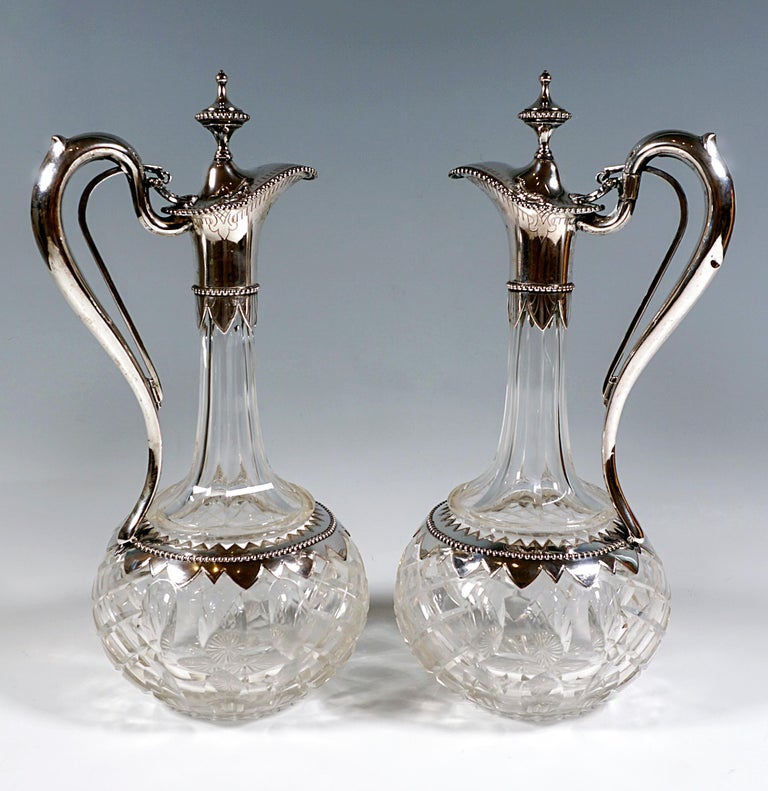 Two carafes made of clear glass with a spherical body on a flush stand with an incised bottom star, the surface alternately decorated with a cut diamond pattern and olive carving and dividing the body into six vertical segments, slightly raised,