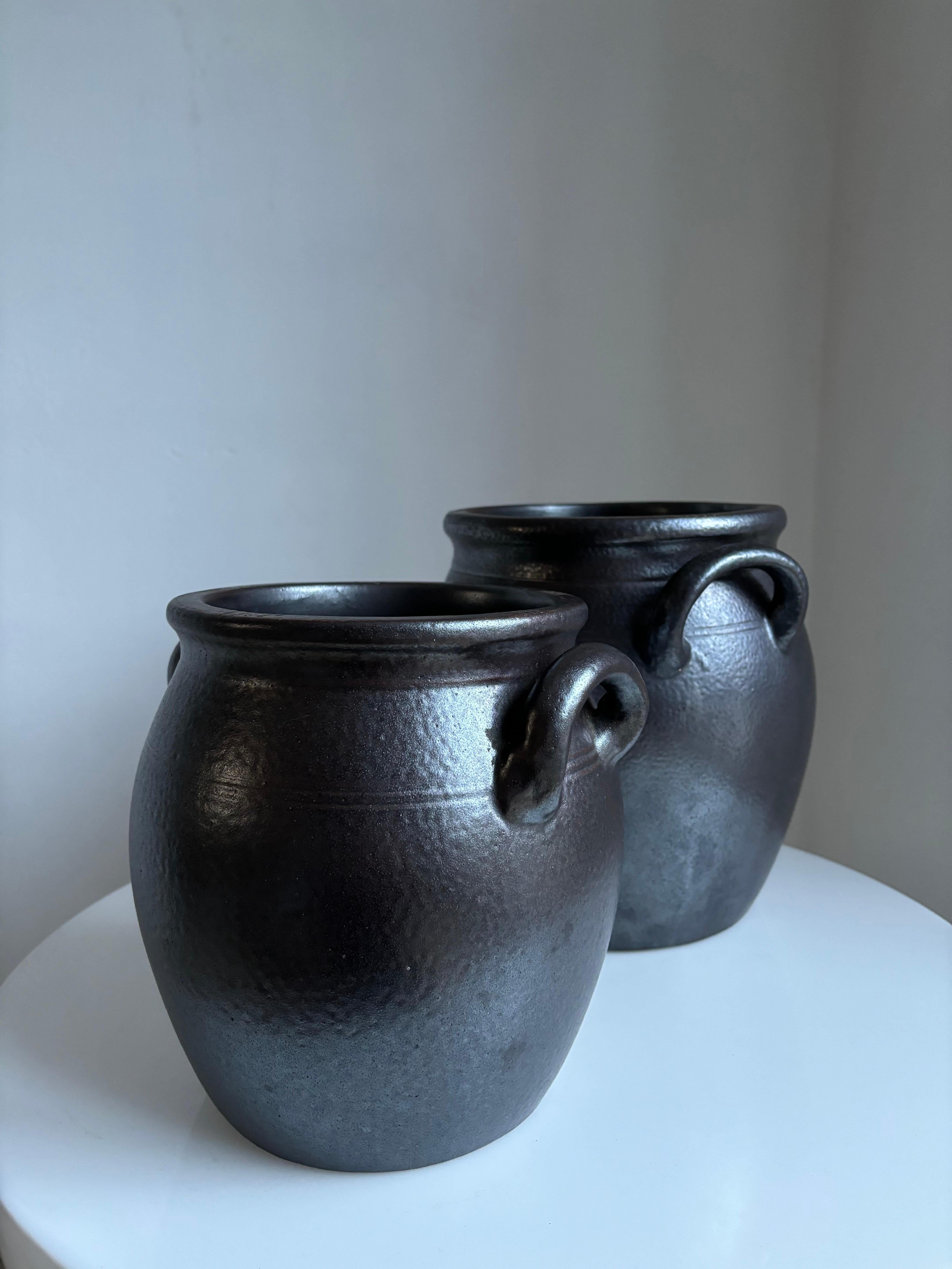 Set of two handmade potbellied stoneware jars with blackish umber brown salt glaze and two soft shaped handles. Manufactured at Höganäs Keramik in Sweden in the 1950s. Two rustic decorative midcentury items originally meant for food storage.