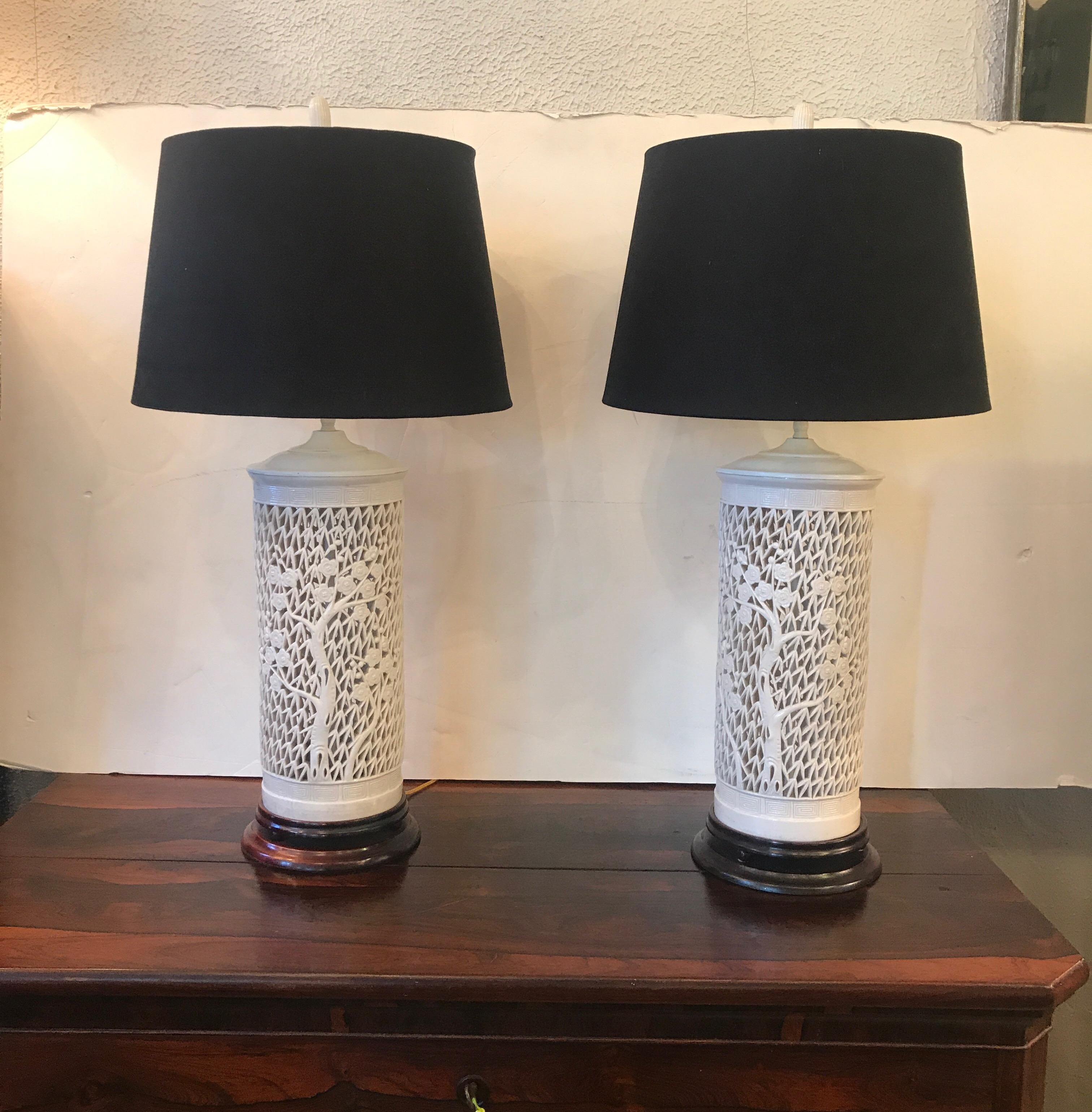 Stunning pair of Hollywood Regency Asian inspired reticulated Blanc de Chine table lamps, circa 1950s. This incredible pierced porcelain pair of lamps accentuated with foliate decoration is mounted on an ebonized base and wired with brass fittings.