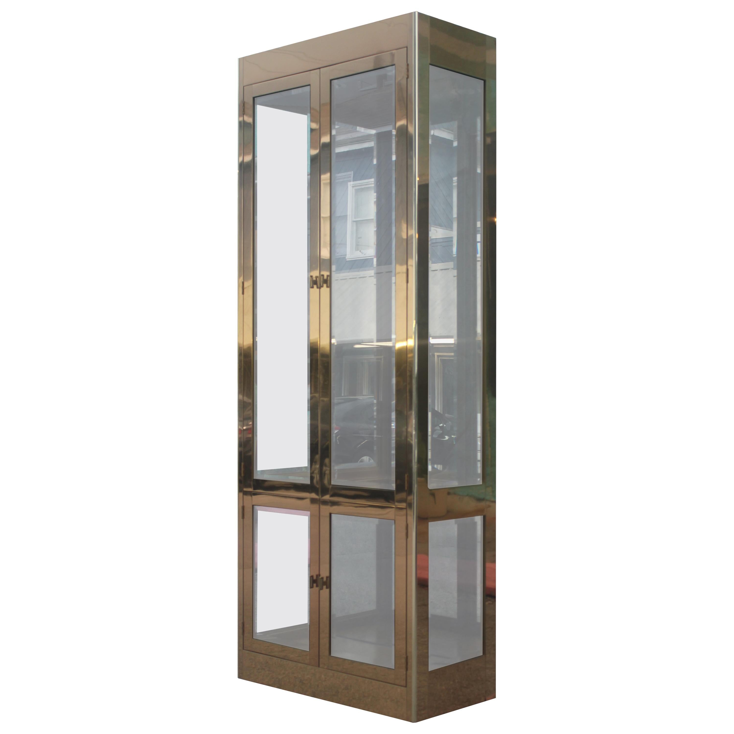Pair of gorgeous Hollywood Regency brass and glass vitrines / bookcases by Mastercraft. Both feature two cabinet spaces (large on top, small on bottom) with adjustable glass shelves.