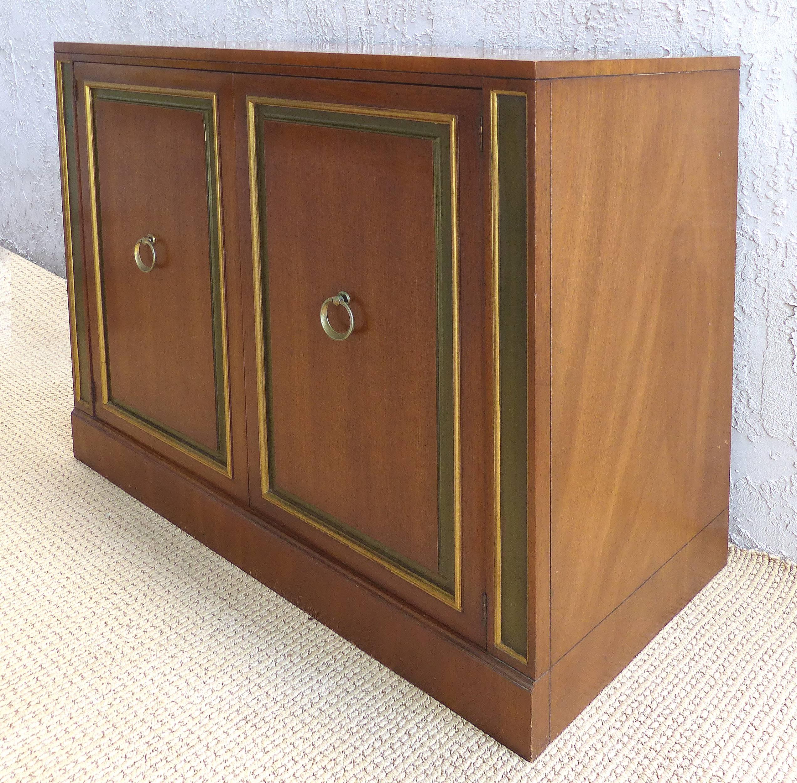 Offered for sale is an elegant pair of 1950s Hollywood Regency cabinets by Dorothy Draper for Heritage Furniture. The pair can be installed as bedside tables or used as servers. The pair retains the original finishes including the gold and olive