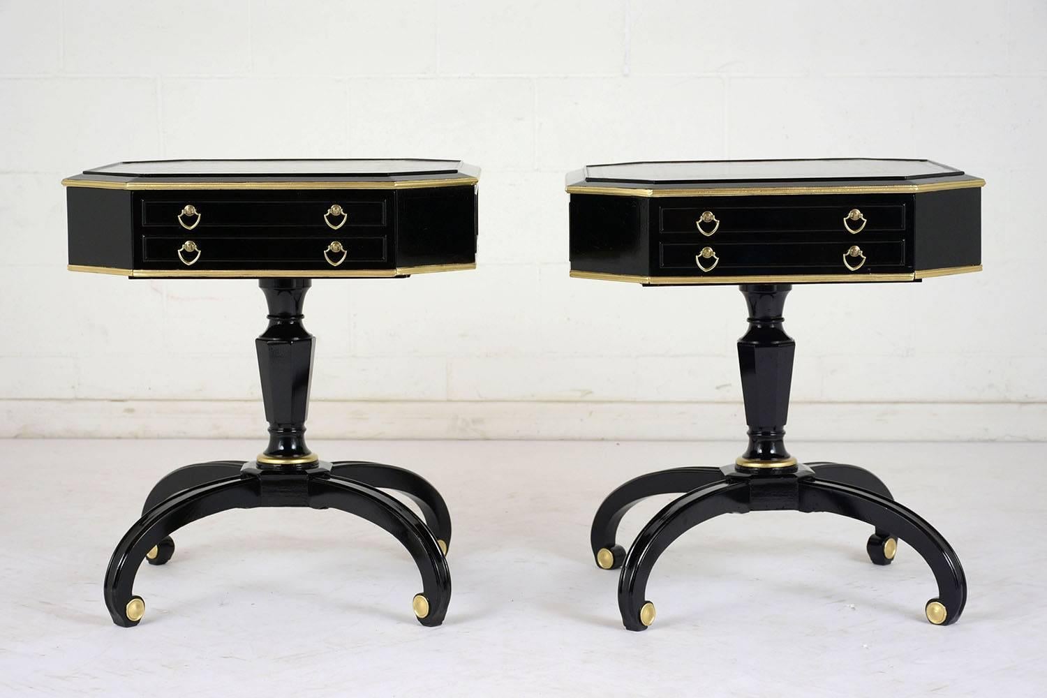 This pair of 1930s Regency-style side tables are made from mahogany wood with an ebonized and lacquered finish. The tables have an octagonal shape with brass moulding accents and a single drawer with brass pulls. On the top of the tables is a dark