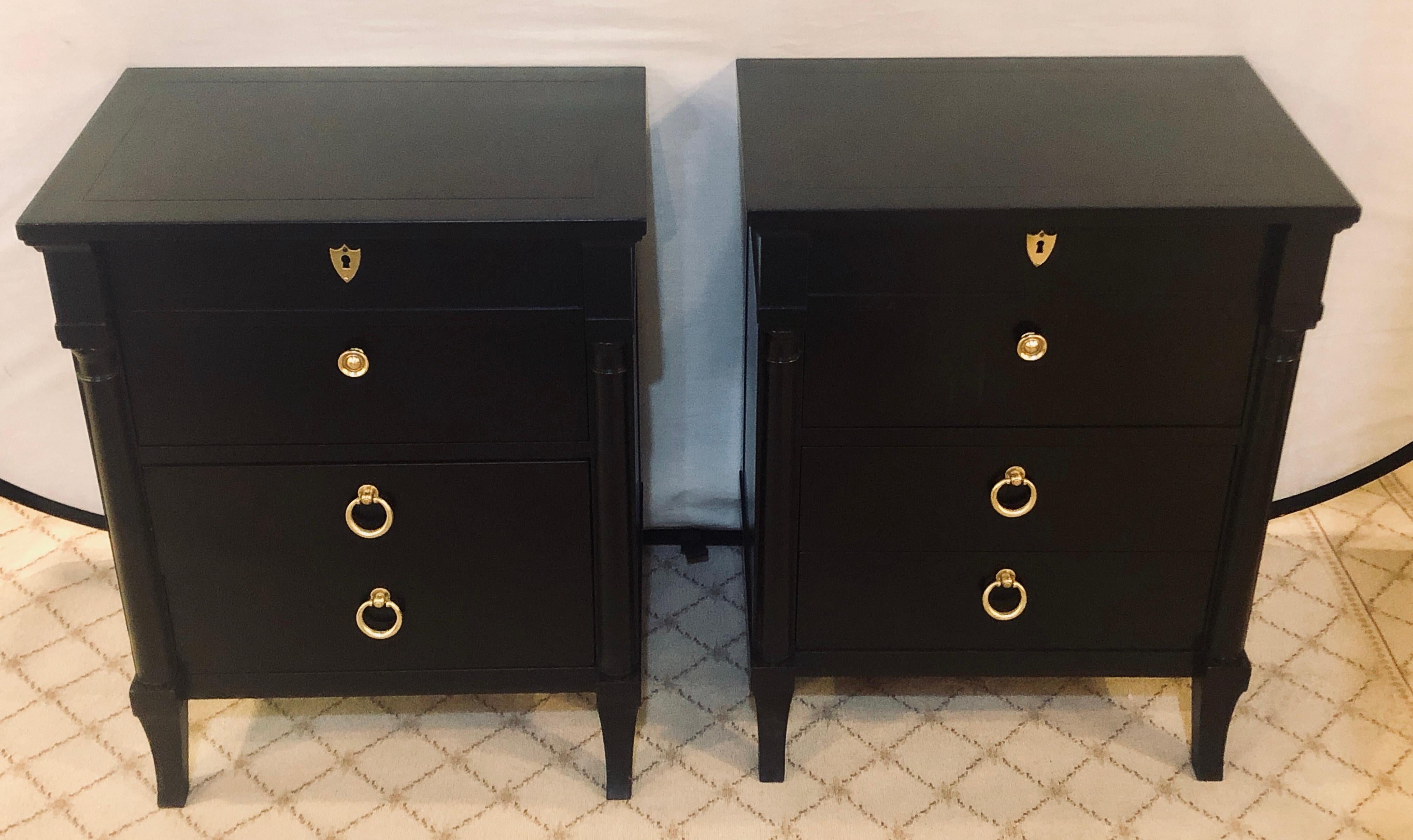 Pair of ebony drop front two-drawer nightstands or end tables in the Hollywood Regency fashion. Each having been fully restored and refinished with bronze pulls and key holes. Both having column form sides.