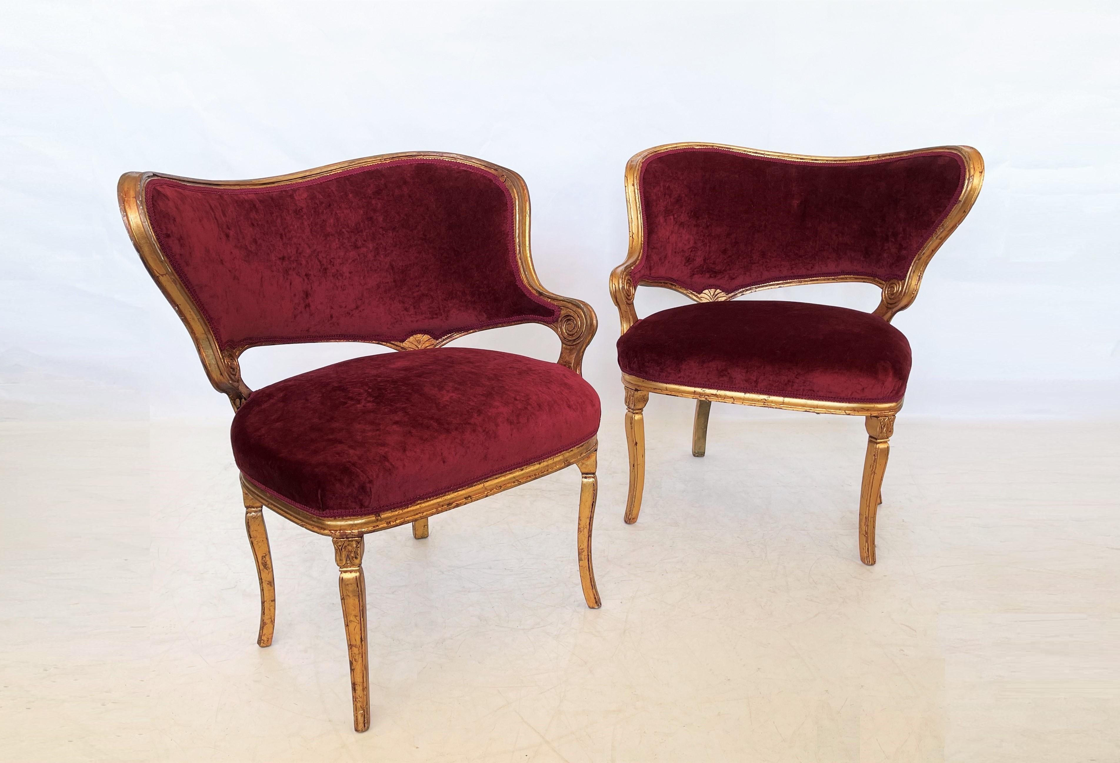 Elegantes Paar spiegelbildlicher, asymmetrischer Art-Déco-Salonstühle mit weinfarbener Polsterung. Das Paar zeichnet sich durch Massivholzrahmen mit Blattgold-Finish, geschwungene Rückenlehnen, konische Beine, geriffelte Schnitzereien und eine sehr