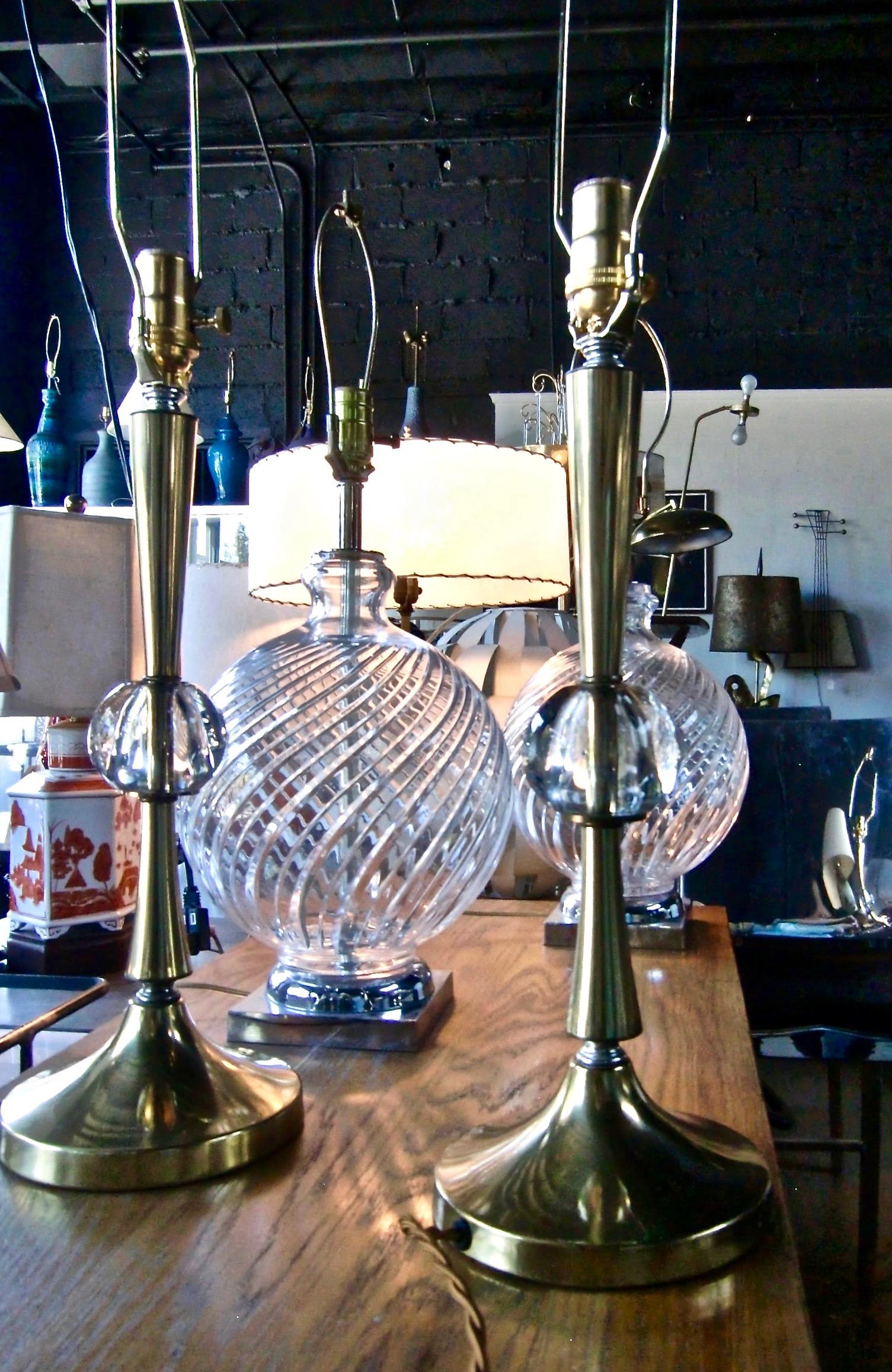 Pair of American crafted Brass and transparent round Crystal Ball Table Lamps. Featuring a corseted and reflective fluted smooth brass stem with clear solid crystal ball center detail, on a circular Brass plated base. Bright. Timeless. Small