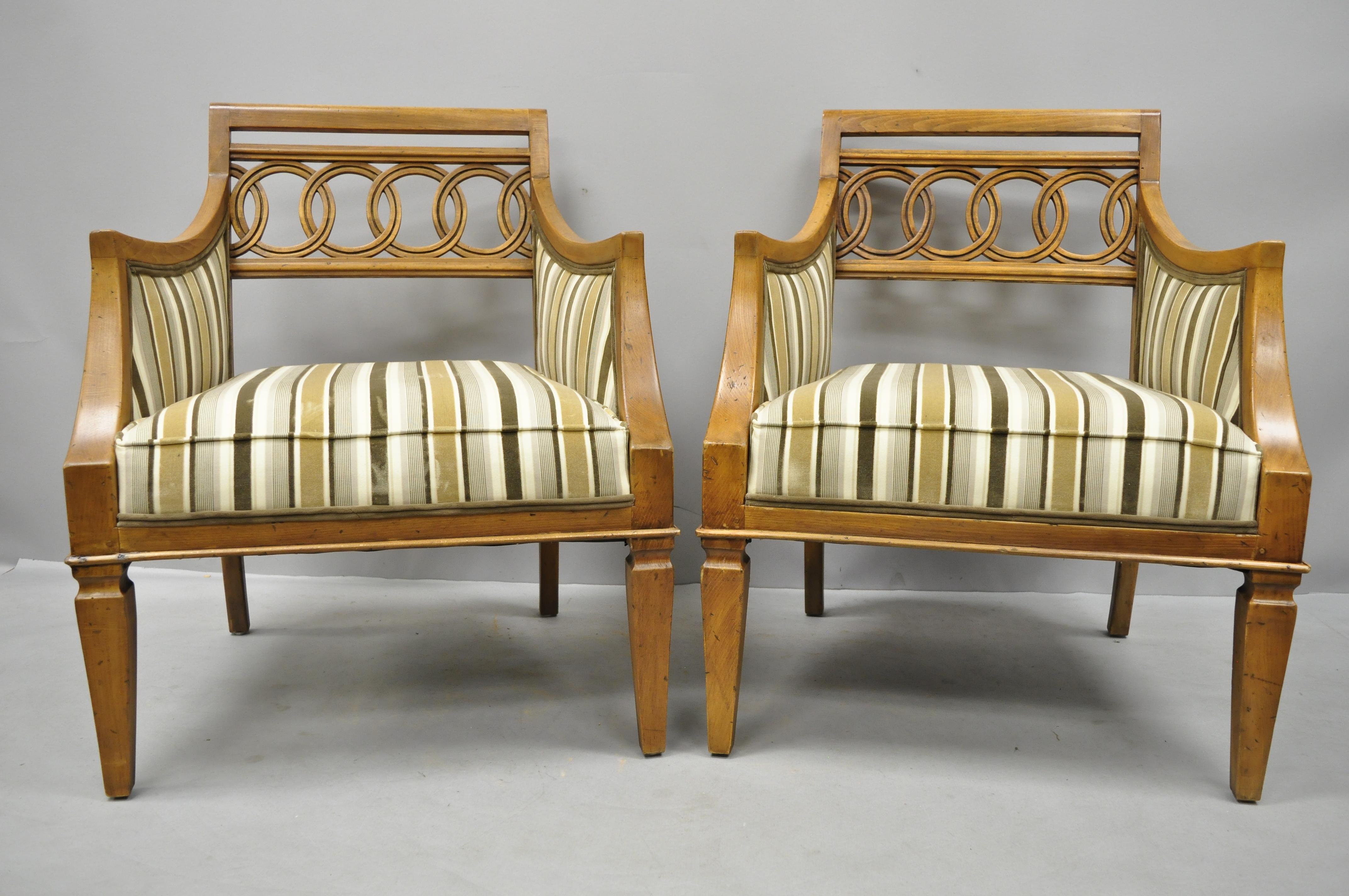 Pair of Hollywood Regency French style carved spiral back armchairs. Items feature striped upholstered seats, carved backs, solid wood construction, beautiful wood grain, distressed finish, tapered legs, sleek sculptural form, circa late 20th