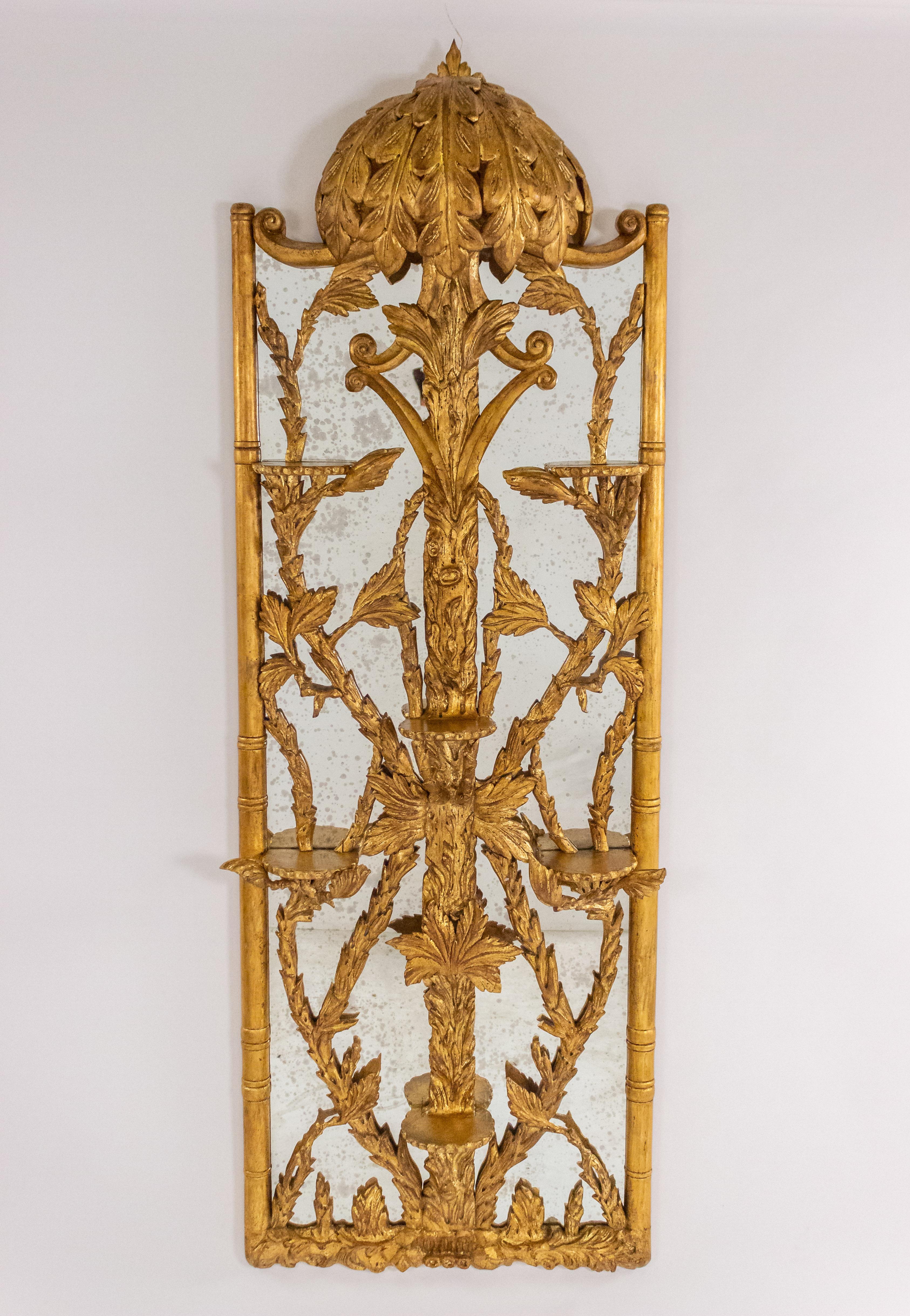Pair of Similar Hollywood Regency gilt mirrors with a carved palm leaf pediment that extends into a canopy above six elaborate shelves connected by tree carvings within a bamboo-design frame.