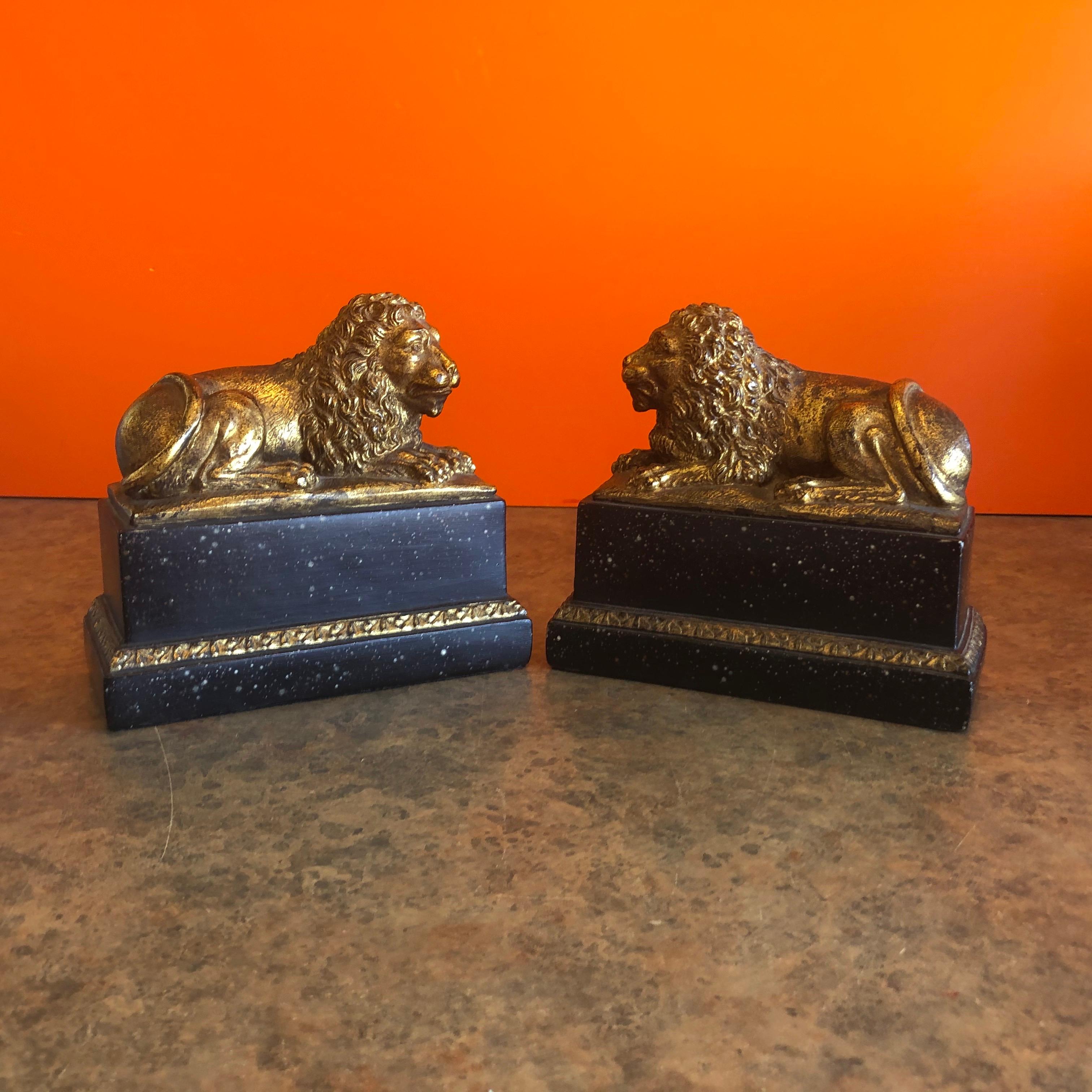 Stunning pair of majestic lion bookends in a gold gilt finish on a faux black marble base by Borghese of Italy, circa 1960s. The pair is in great vintage condition and our made of cast plaster with a built in metal slide to go under the books. #1192.