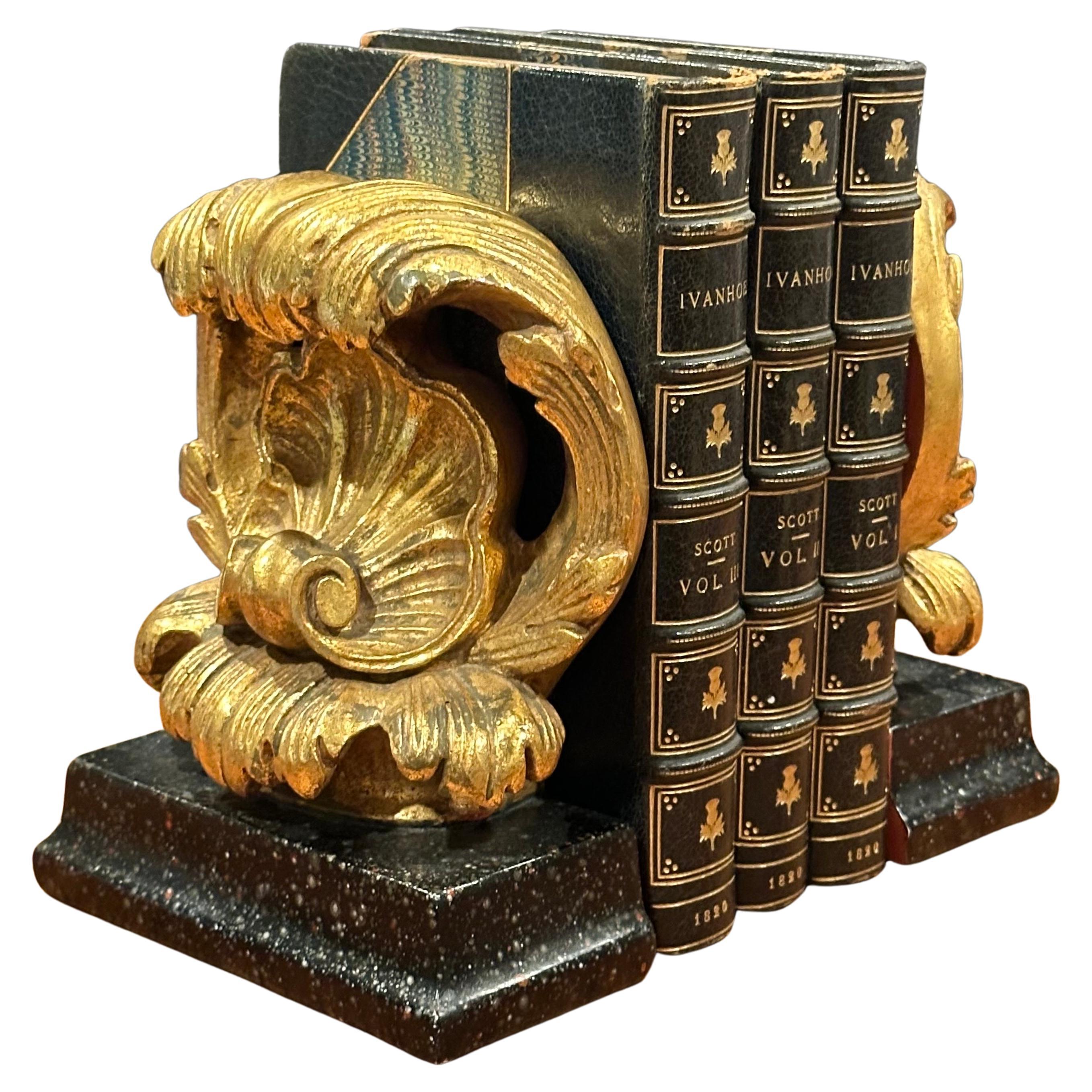 Splendida coppia di maestosi fermalibri a cartiglio con finitura dorata su una base in finto marmo nero di Borghese, circa anni '50. Sono in ottime condizioni d'epoca e sono realizzati in gesso con uno scivolo metallico incorporato per passare sotto
