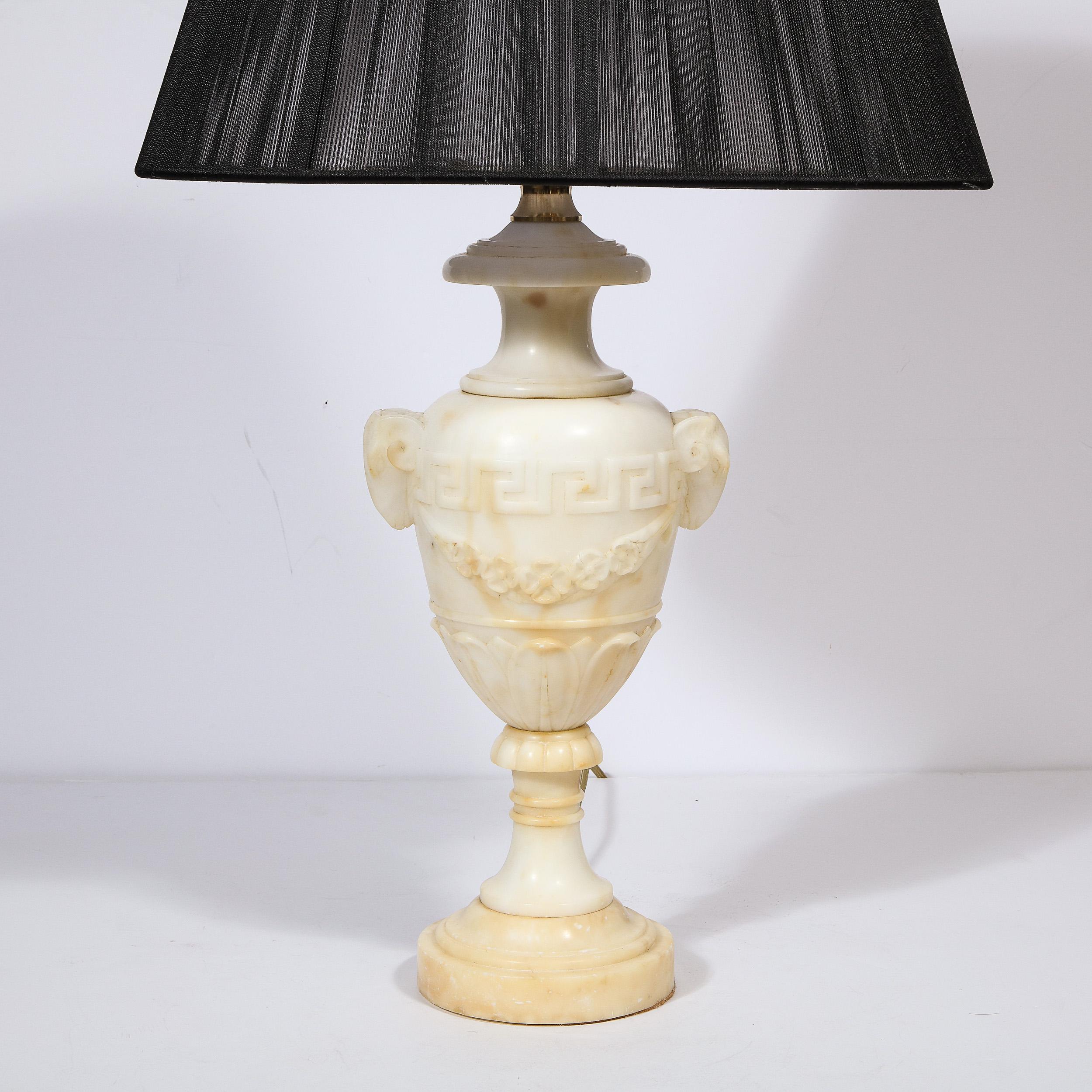 This elegant pair of Hollywood Regency alabaster table lamps were realized in France circa 1940.  Realized in a sumptuous variegated cream hued alabaster, these lamps have been hand carved with a wealth neoclassical details gleaned from ancient