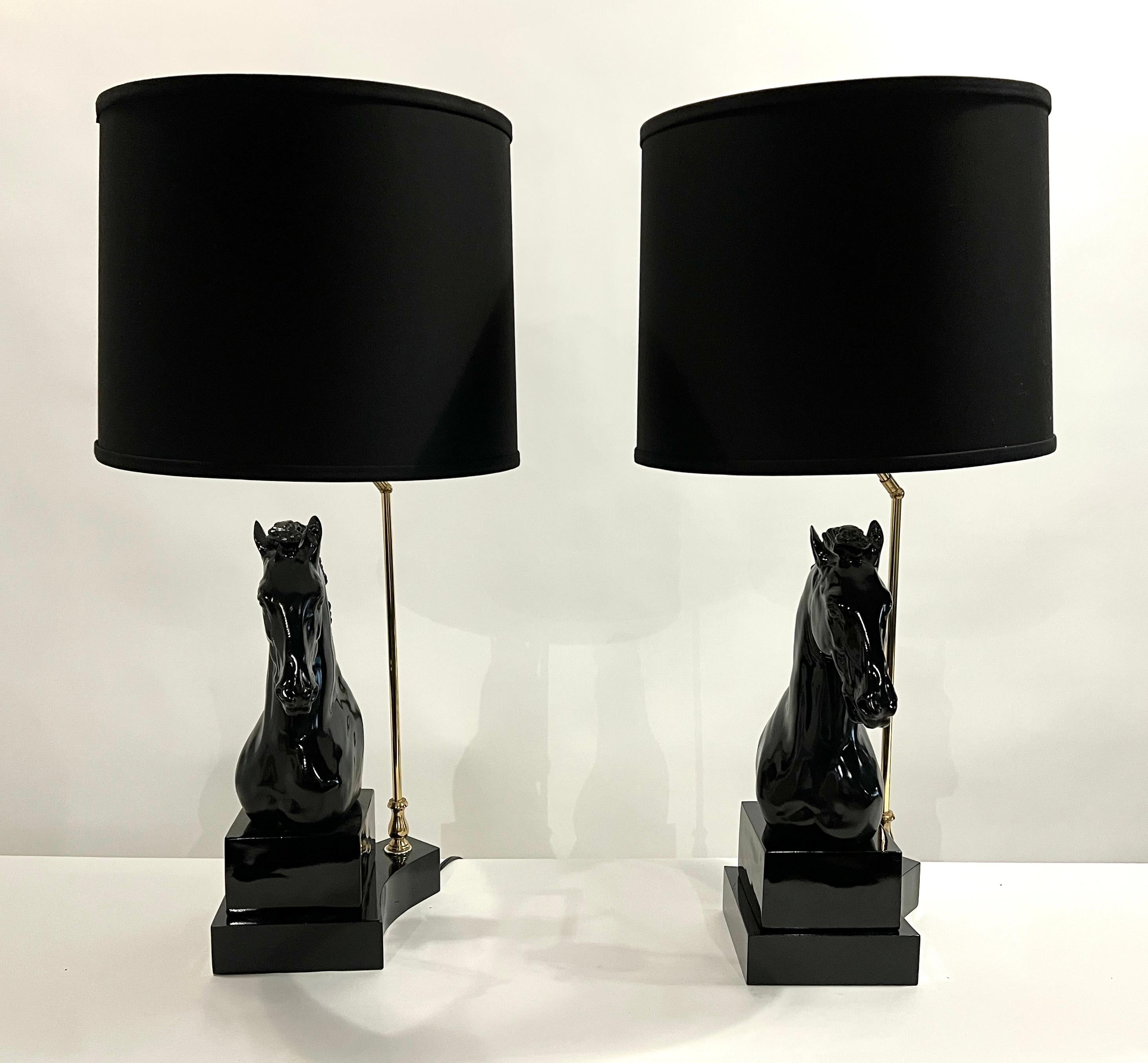 Hollywood Regency style horse head lamps in high glass black lacquer on wood plinths with brass accents. 