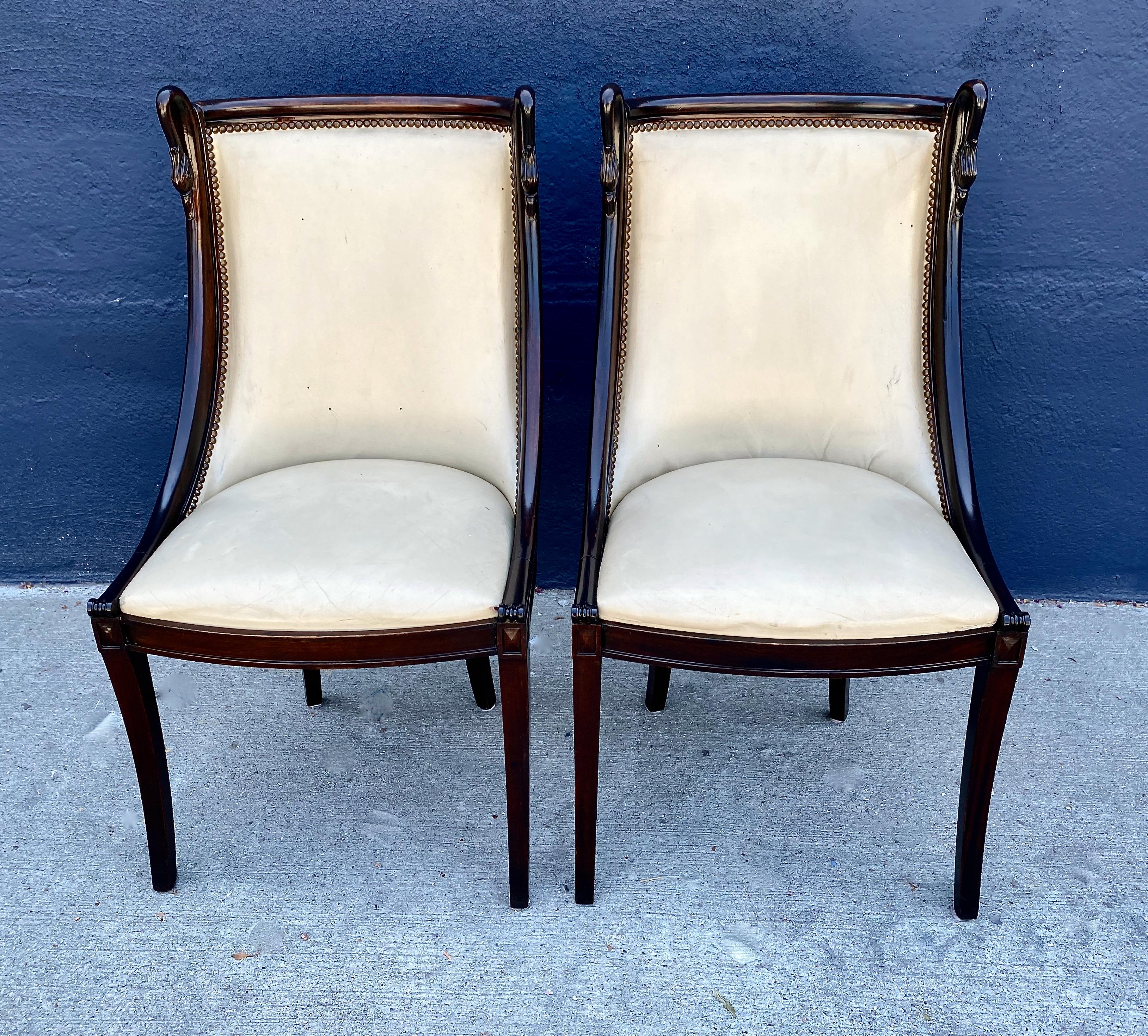 This is a chic pair of carved Mahogany Empire-style Hollywood Regency side chairs that date to the mid-20th century. The modified klismos neoclassical form of these chairs make them a standout; the carved swan detailing to the crest heightens their