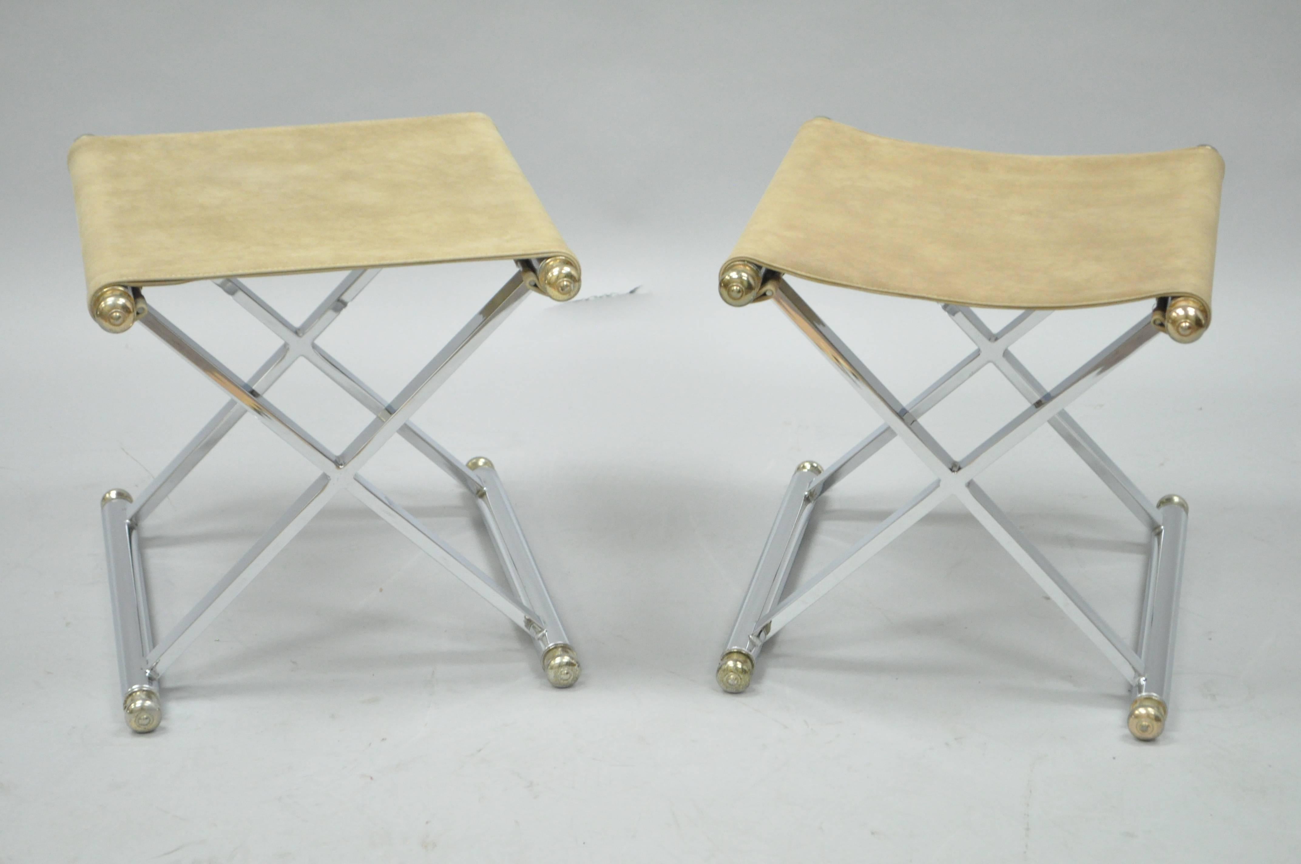 Pair of vintage Hollywood Regency X-base chrome and brass stools in the manner of Maison Jansen. The pair features polished chrome X-form frames, seamless joints, brass tone finials, and original tan suede seats.