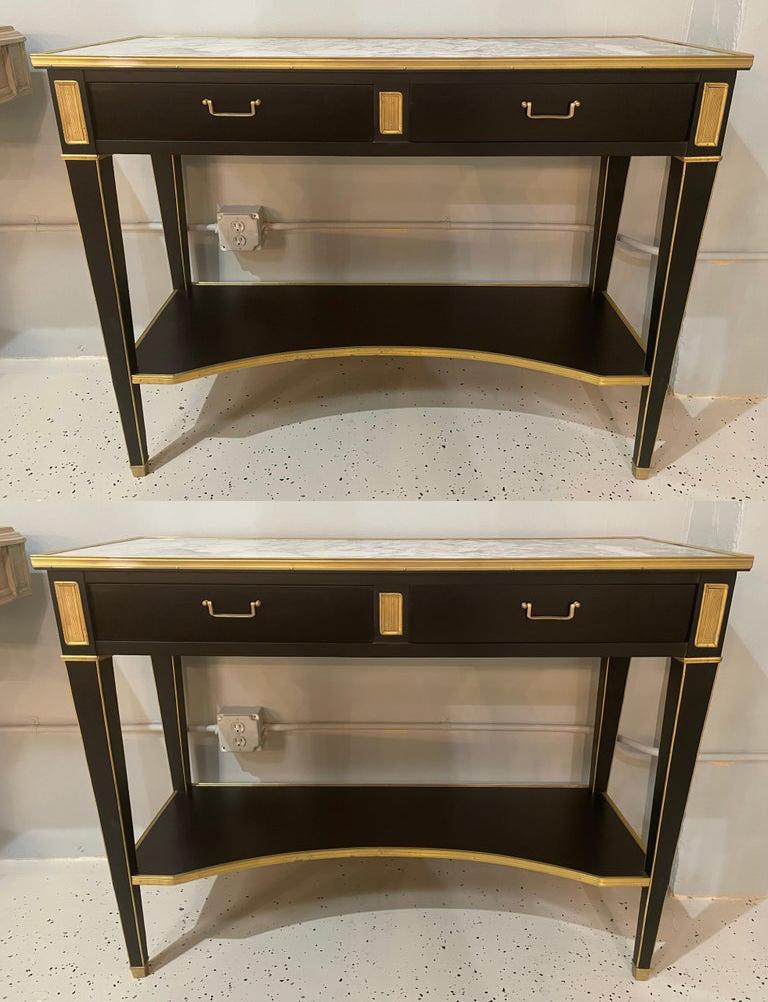 Pair of Hollywood Regency neoclassical ebony console or sofa tables in the manner of Maison Jansen. A stunning sleek and stylish pair of console tables in an ebony finish having a bronze framed marble top supported by a lower case of two drawers