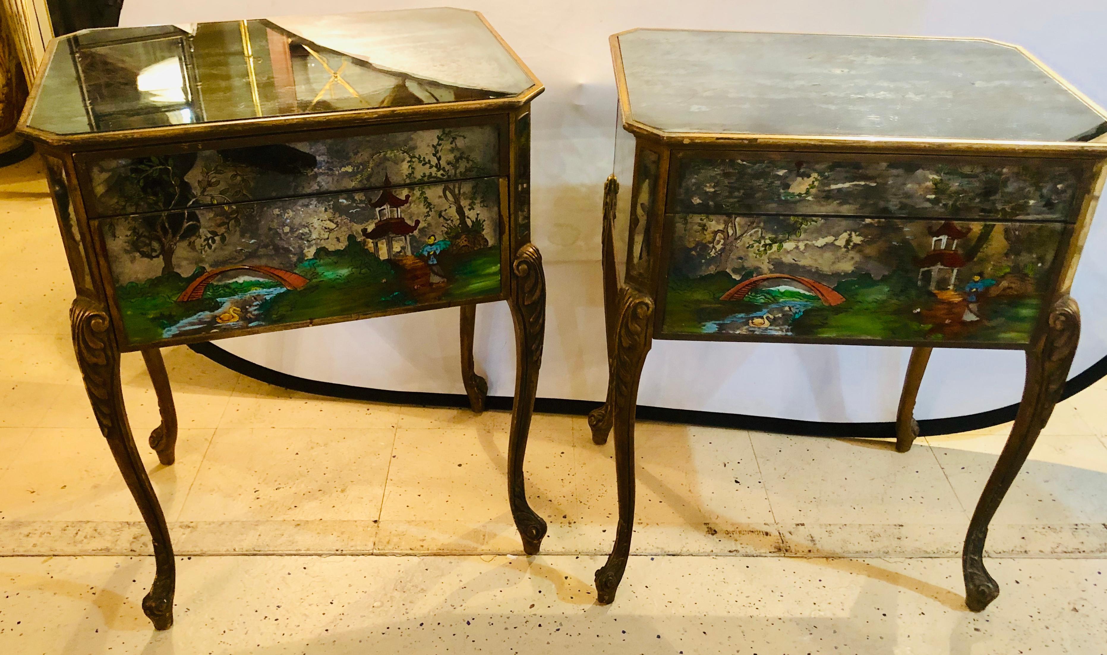 Pair of Hollywood Regency painted end or night tables on mirrored cases. Each having poly-chromed scenes depicting children amid the road leading to their home. The case itself painted decorated in a gilt gold finish and finely carved.