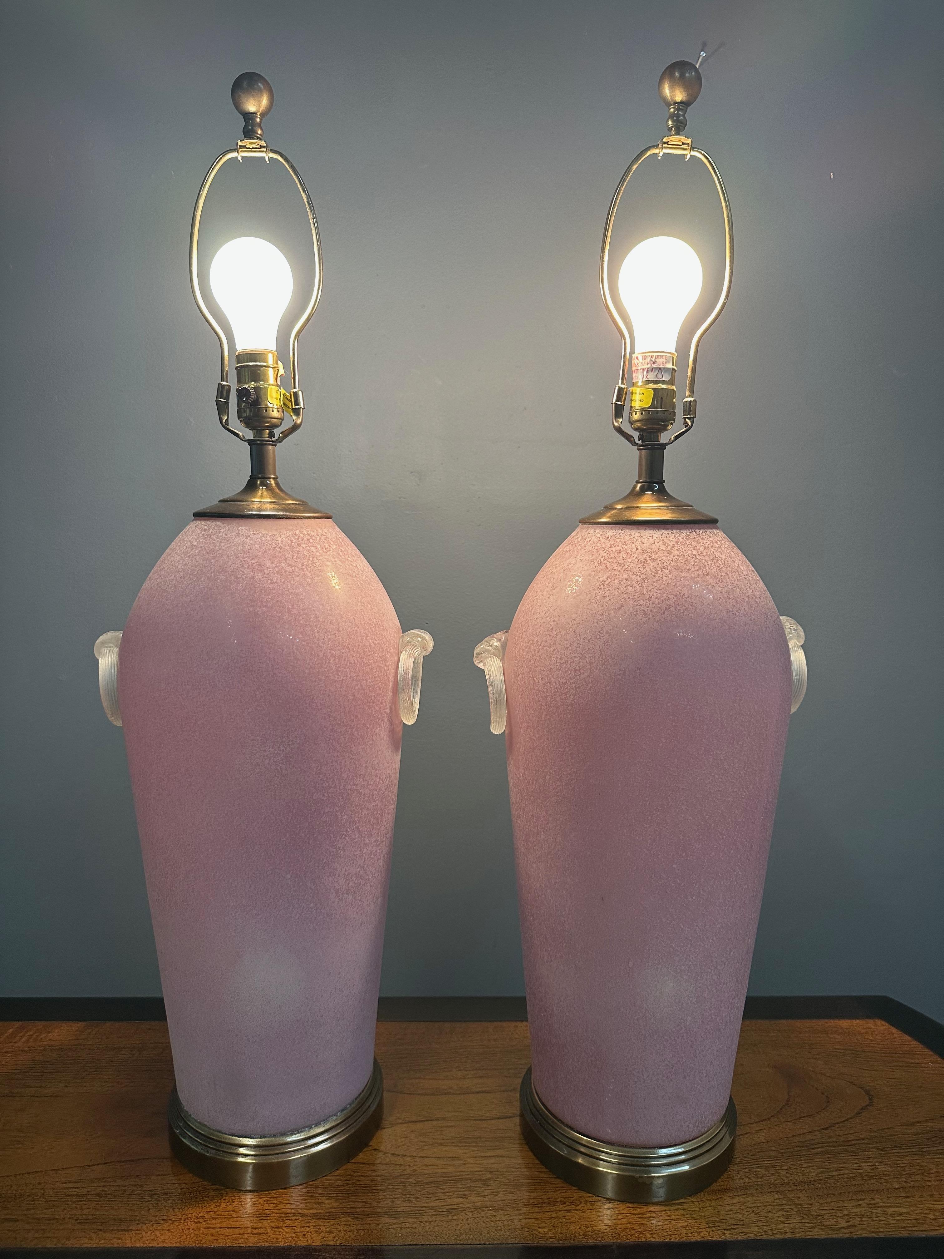 Elegant pair of Mid-Century table lamps featuring softly tapered baluster-form bodies crafted from pink cased glass with a velvety, frosted finish. Each lamp is accented with a sculptural ribbon glass ring mounted on both sides—an unusual and
