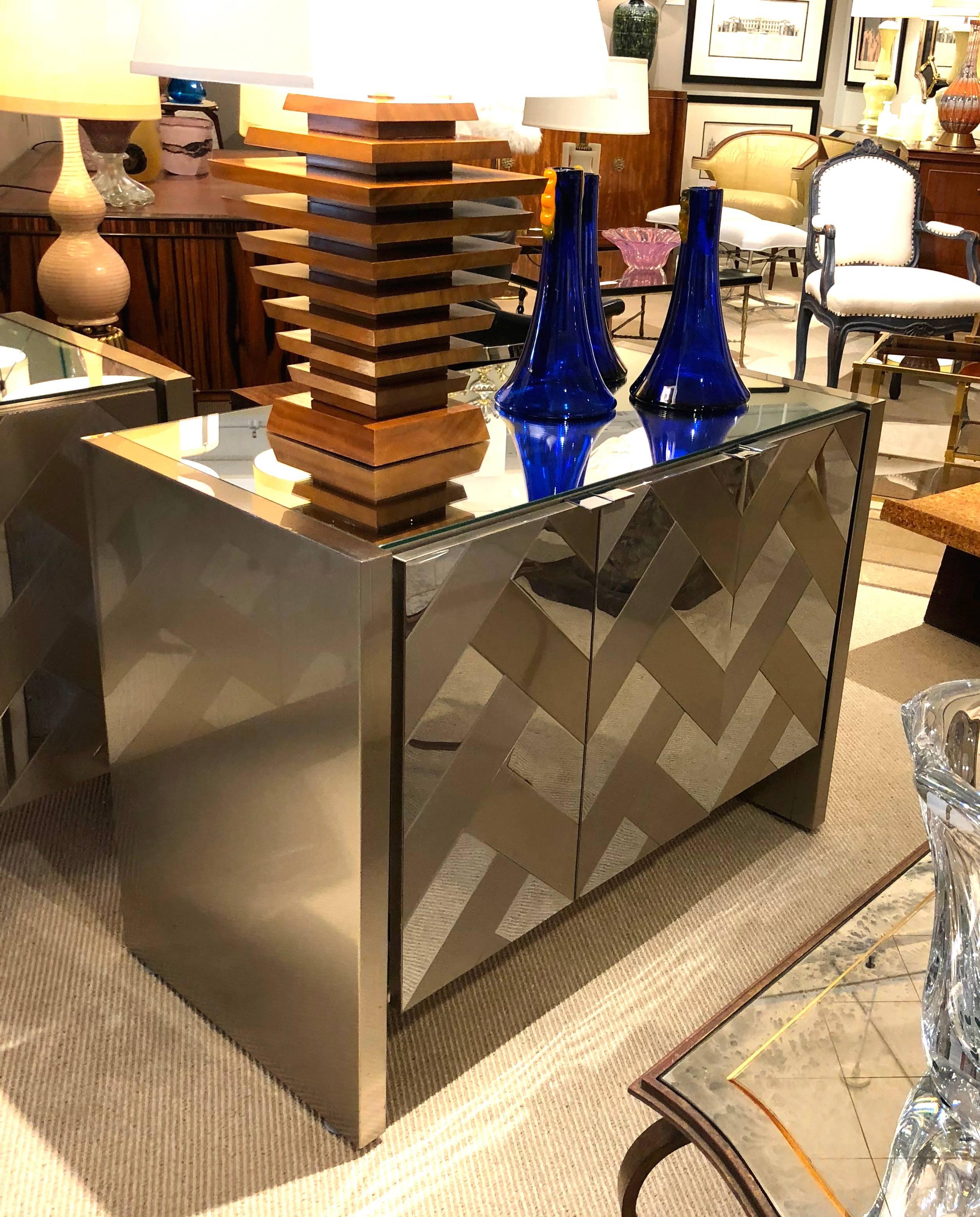 A stylish pair of Hollywood Regency satin brass and polished steel cabinets or chests by Ello; these very chic cabinets with mirrored tops featuring satin brass and polished steel chevron-designed front panels with white laminate interiors fitted