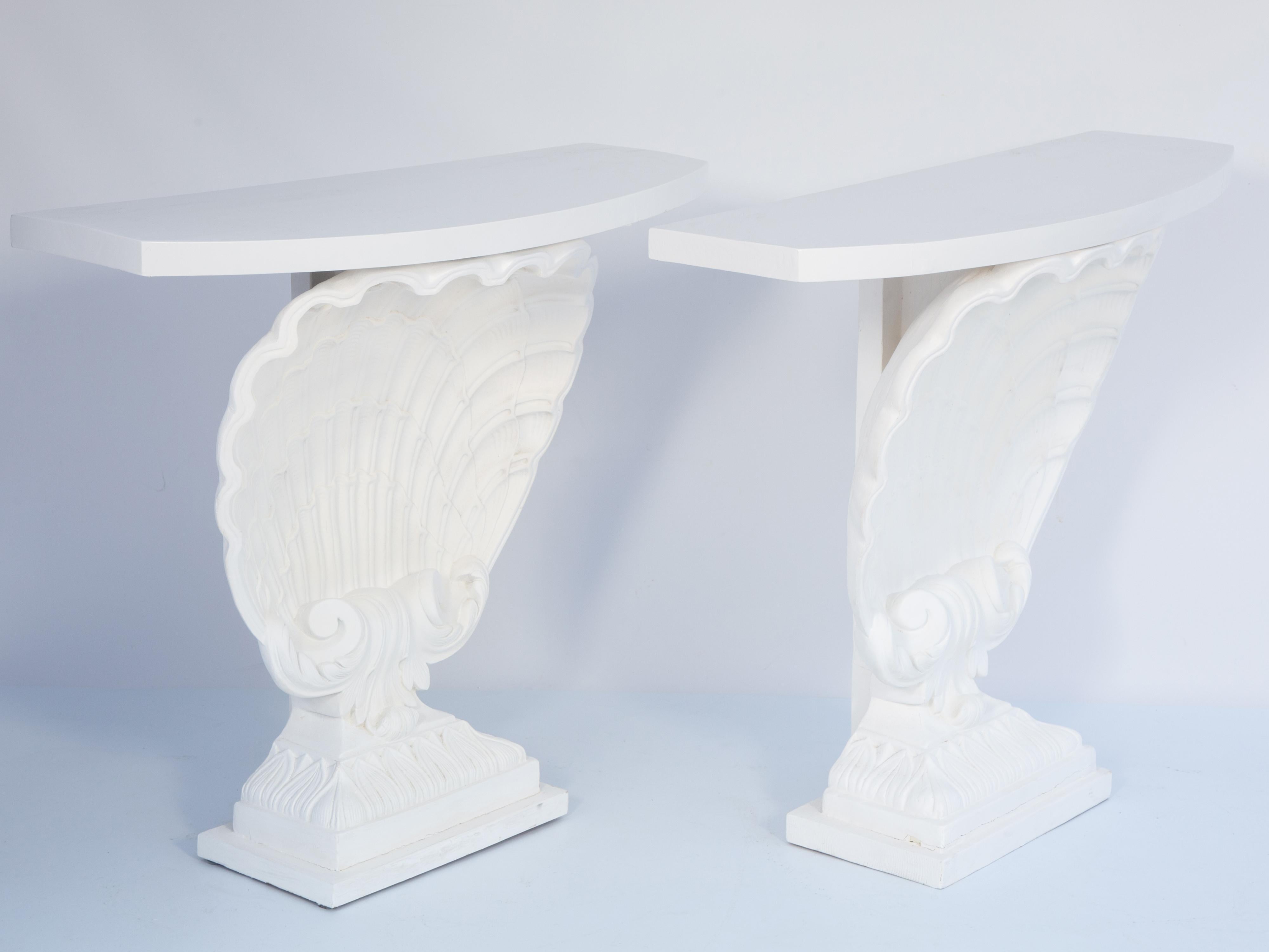 Pair of vintage painted Hollywood Regency console tables manufactured by Grosfeld House, each rectangular top with bowed front, on a painted scallop shell table base of plaster, raised on foliate-decorated graduated plinth base. 

Stock ID: D3855