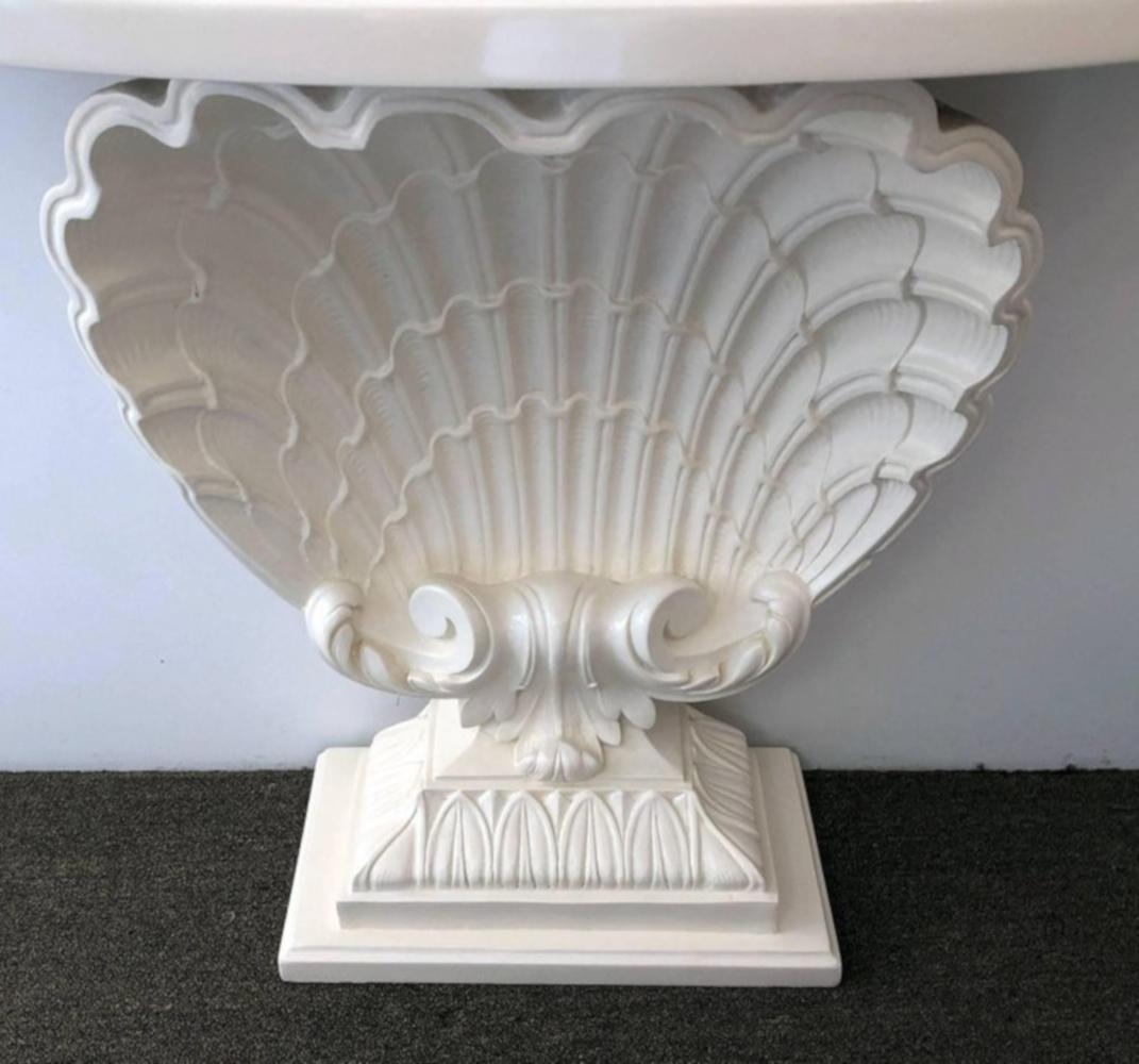 Pair of shell consoles having a cast plaster shell body, with a rounded front top and classical plinth base. We have had these restored and repainted in a matte white. However we can have them re painted for you in a specific color f your choice for