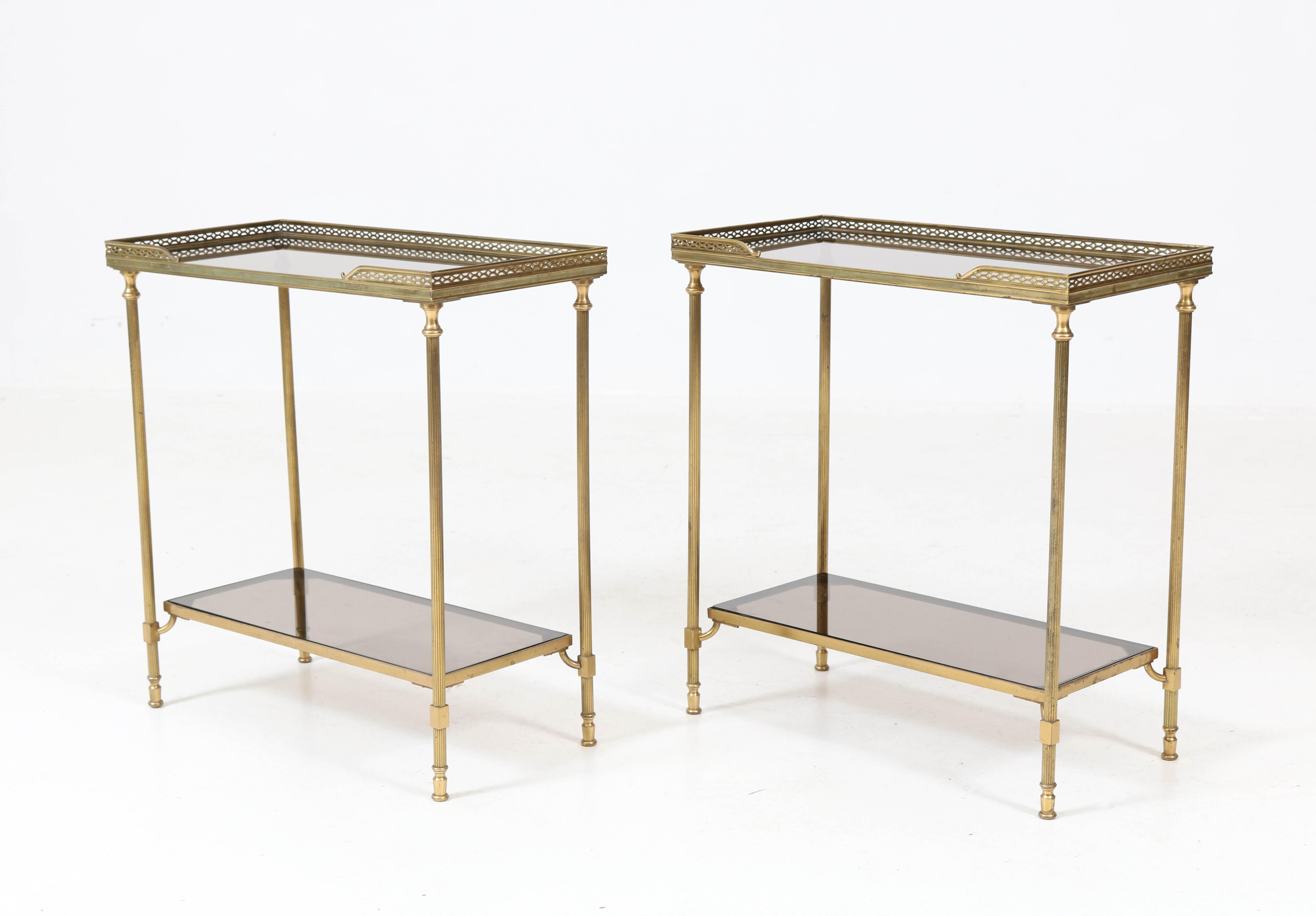 Pair of Hollywood Regency side tables by Maison Jansen, 1970s.
Gilt brass frames with original brown-bluish glass tops.
Minor chip in one of the tops but not to see when placed in the frame.
In good original condition with minor wear consistent