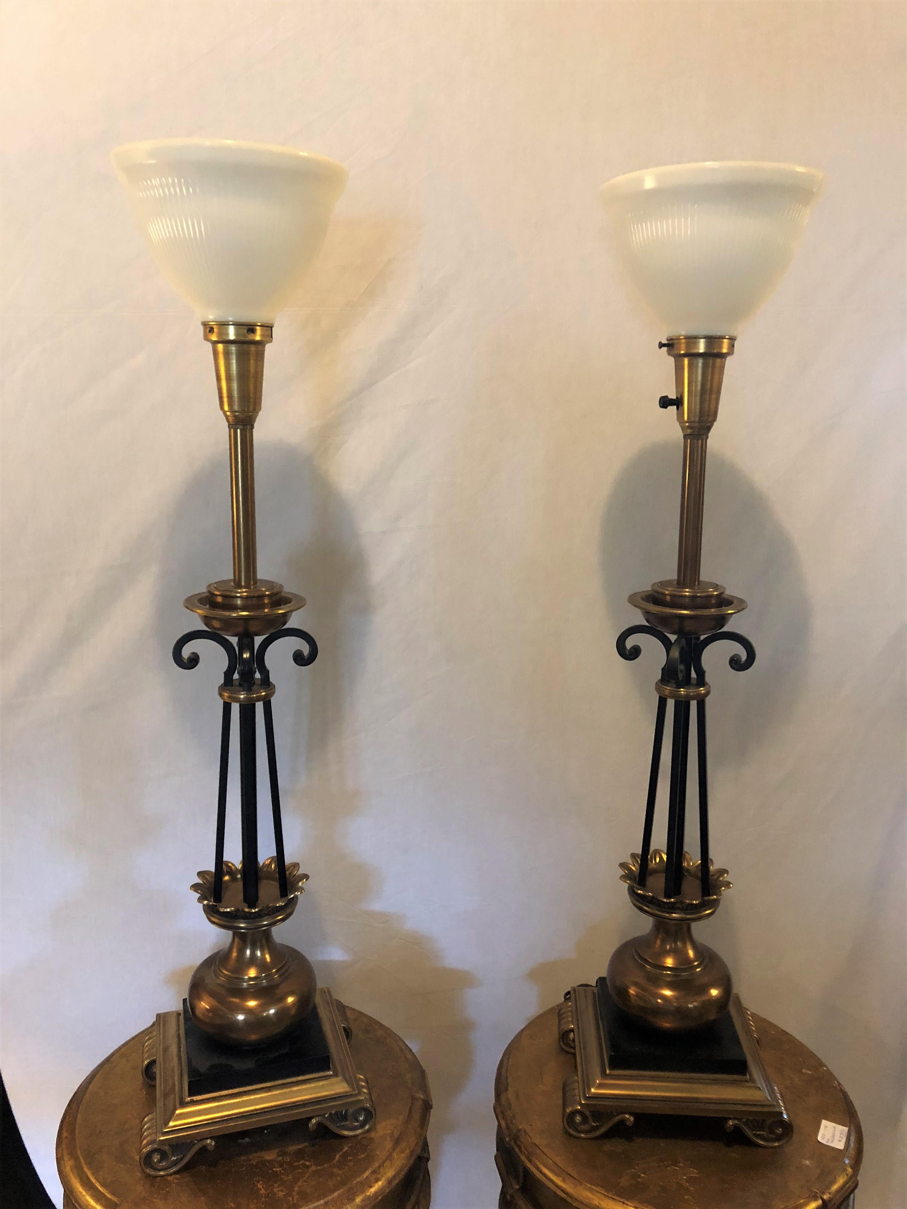 Une paire de lampes de table en forme de colonne de Stiffel Co. en laiton et ébénisé, chacune signée. Chacune d'entre elles est réalisée dans le style Hollywood Regency, avec un design en métal, laiton et ébène, et des globes en verre laiteux.