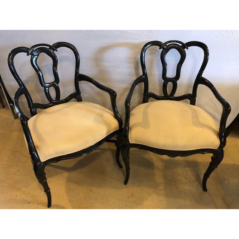 An elegant pair of carved wood lacquer bamboo form pretzel back armchairs in a slick ebony finish. The pair features an off -white quality upholstery making it very comfortable and stylish at the same time. These timeless custom quality arm chairs