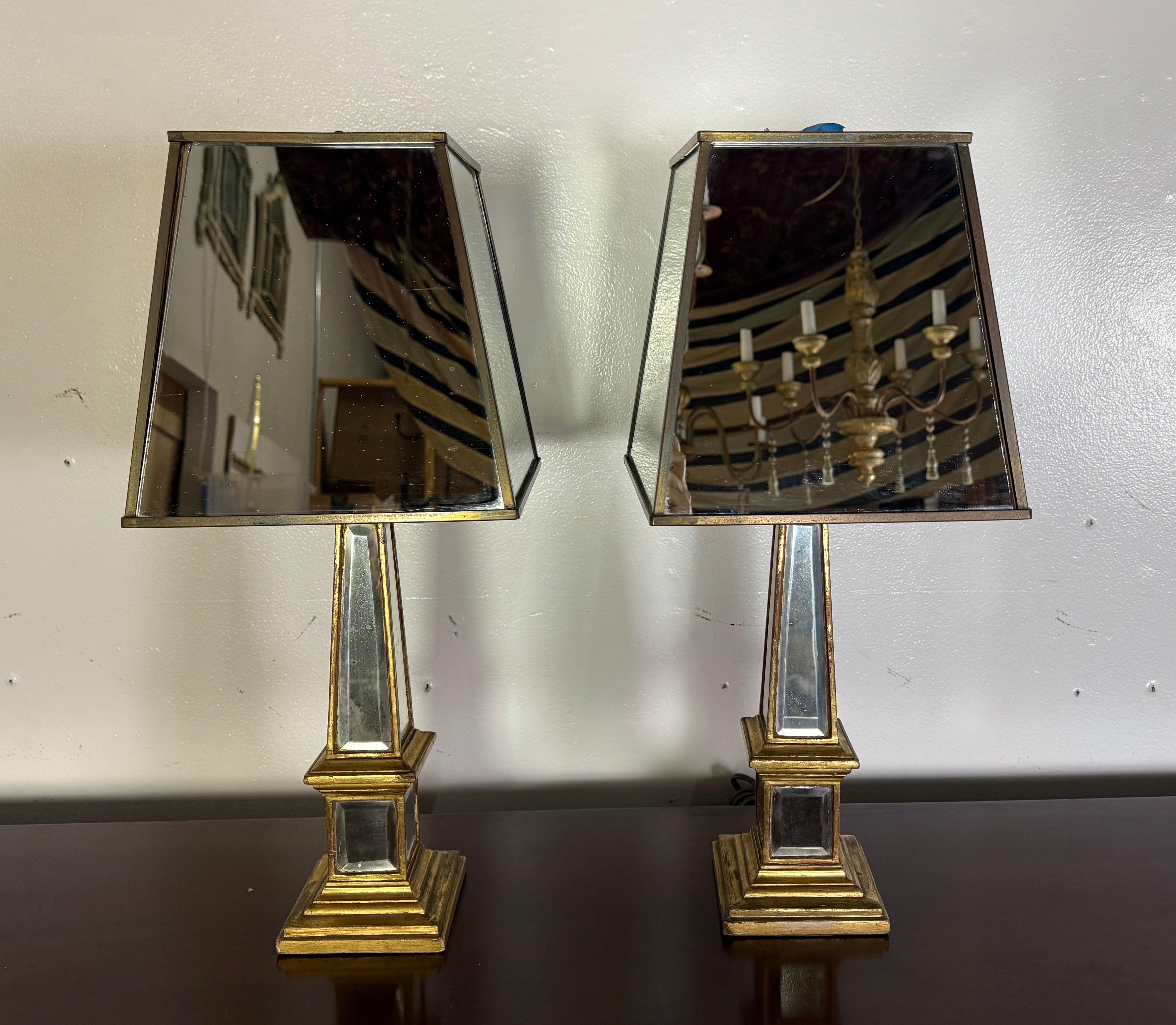 Este llamativo par de lámparas de espejo de los años 60 ejemplifica el estilo de la Regencia de Hollywood con su atrevida geometría y sus glamurosos materiales. Cada lámpara tiene una base en forma de obelisco adornada con paneles de espejo biselado