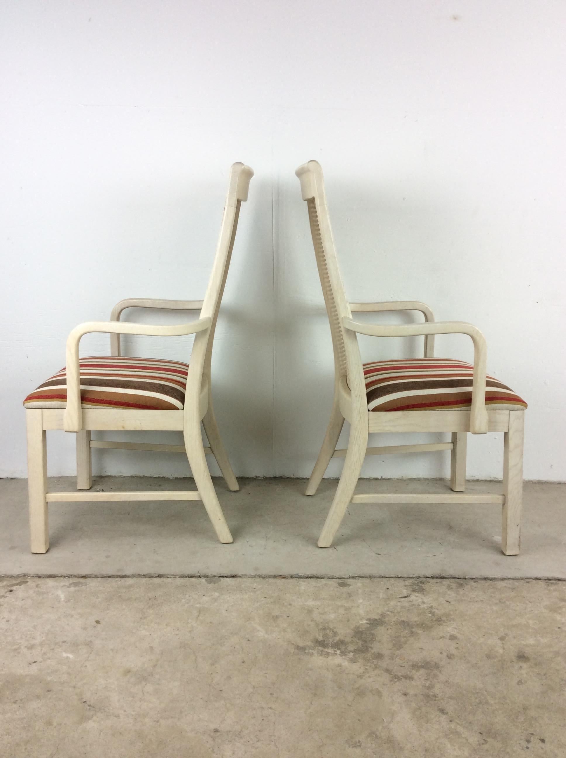 This pair of dining chairs features hardwood construction, original white wash finish, cane backed seats, vintage red brown white striped upholstery, sculpted wood arm rests and tall tapered legs.  

Complimentary lounge chair available