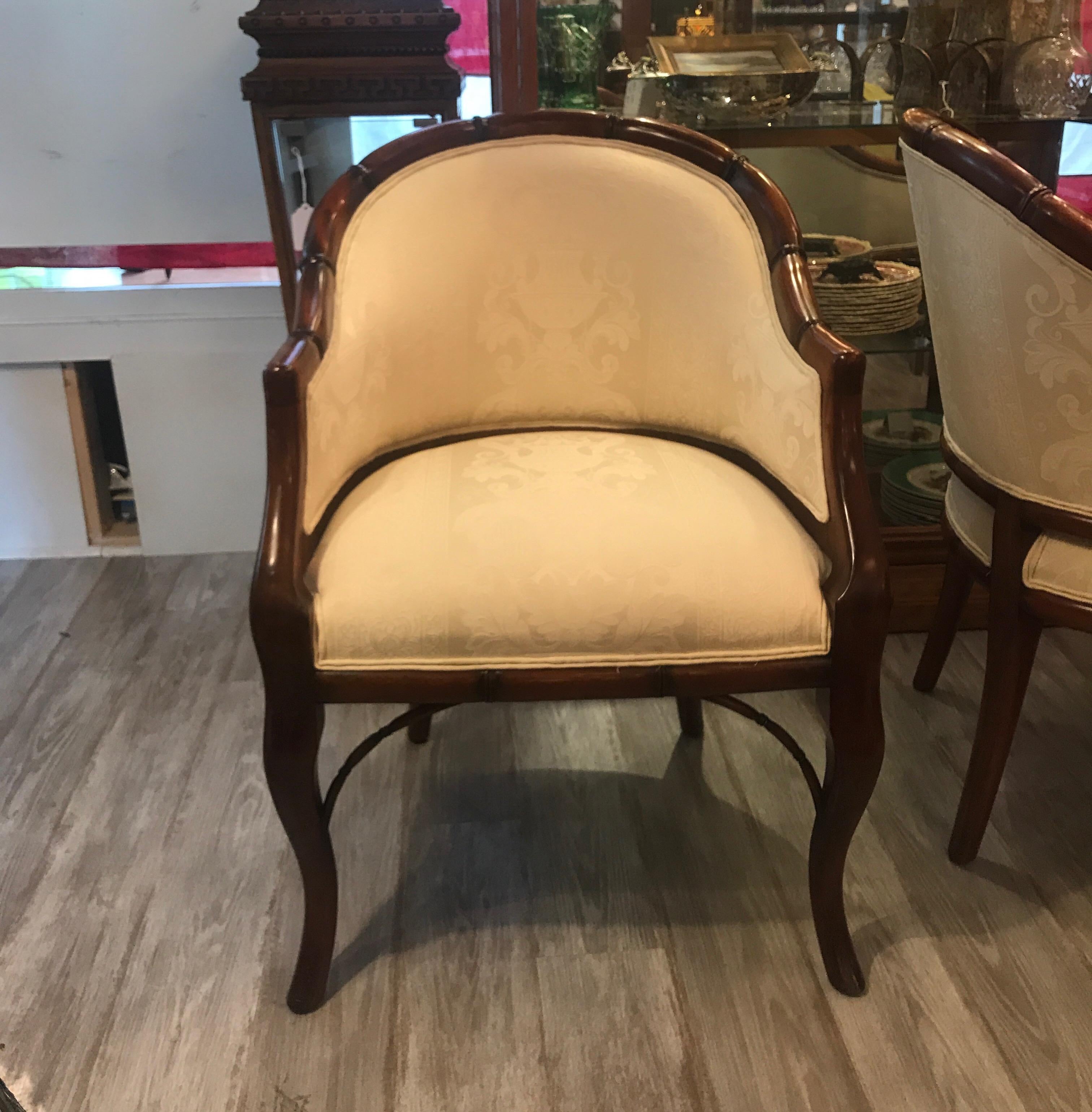 A pair of walnut faux bamboo rounded back tub chairs with ivory tone on tone damask upholstery. The smaller accent chairs with a comfortable seat and back with nicely curved legs.