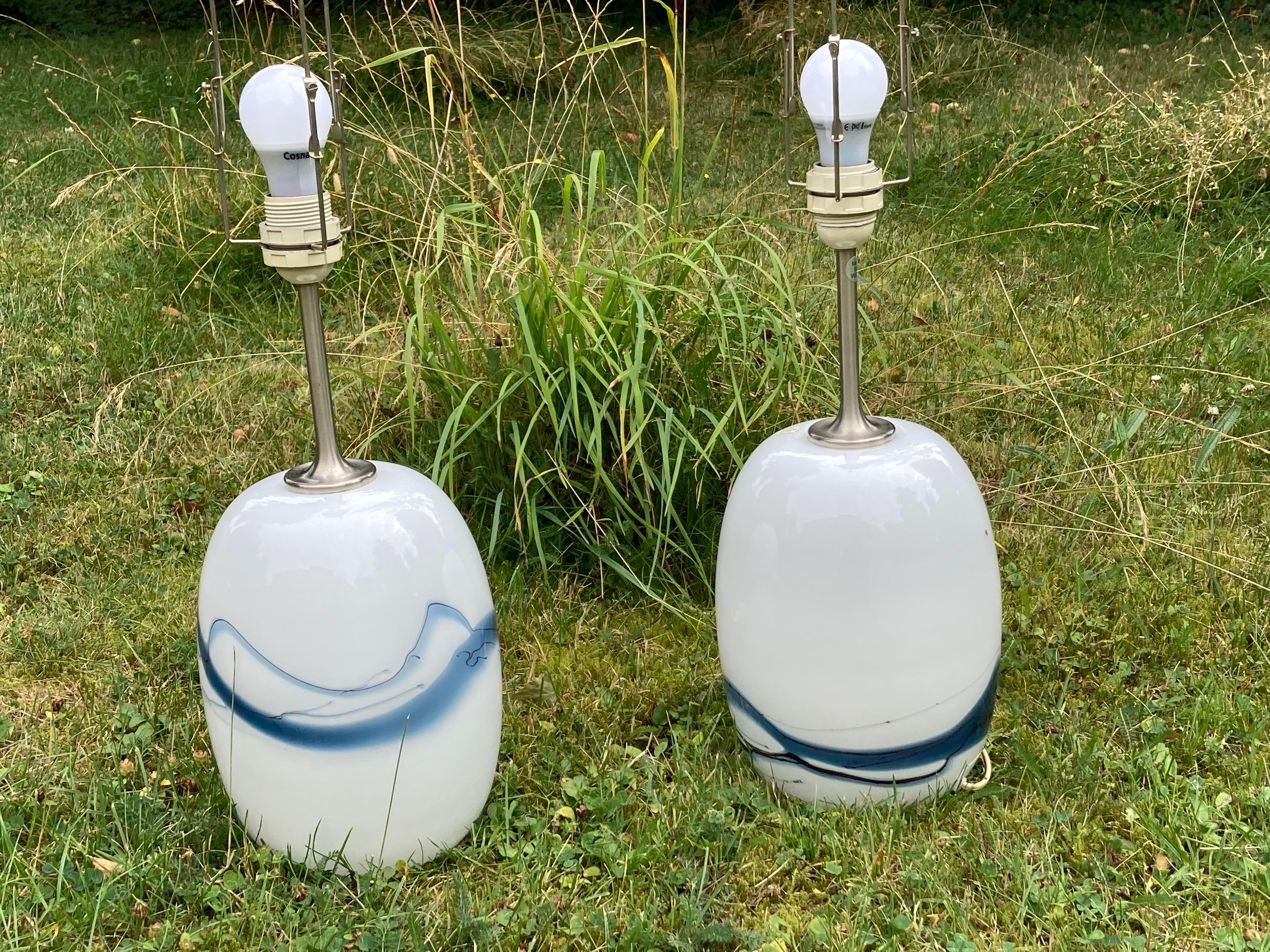 Zwei Holmegaard-Lampen mit gebürsteten Stahlbeschlägen von Holmegaard, Dänemark, 1984, in Weiß mit einer Vielzahl von blauen Glasschmelzen unter dem glatten Klarglas, entworfen von Michael Bang, 1984.
Die Höhe von 14