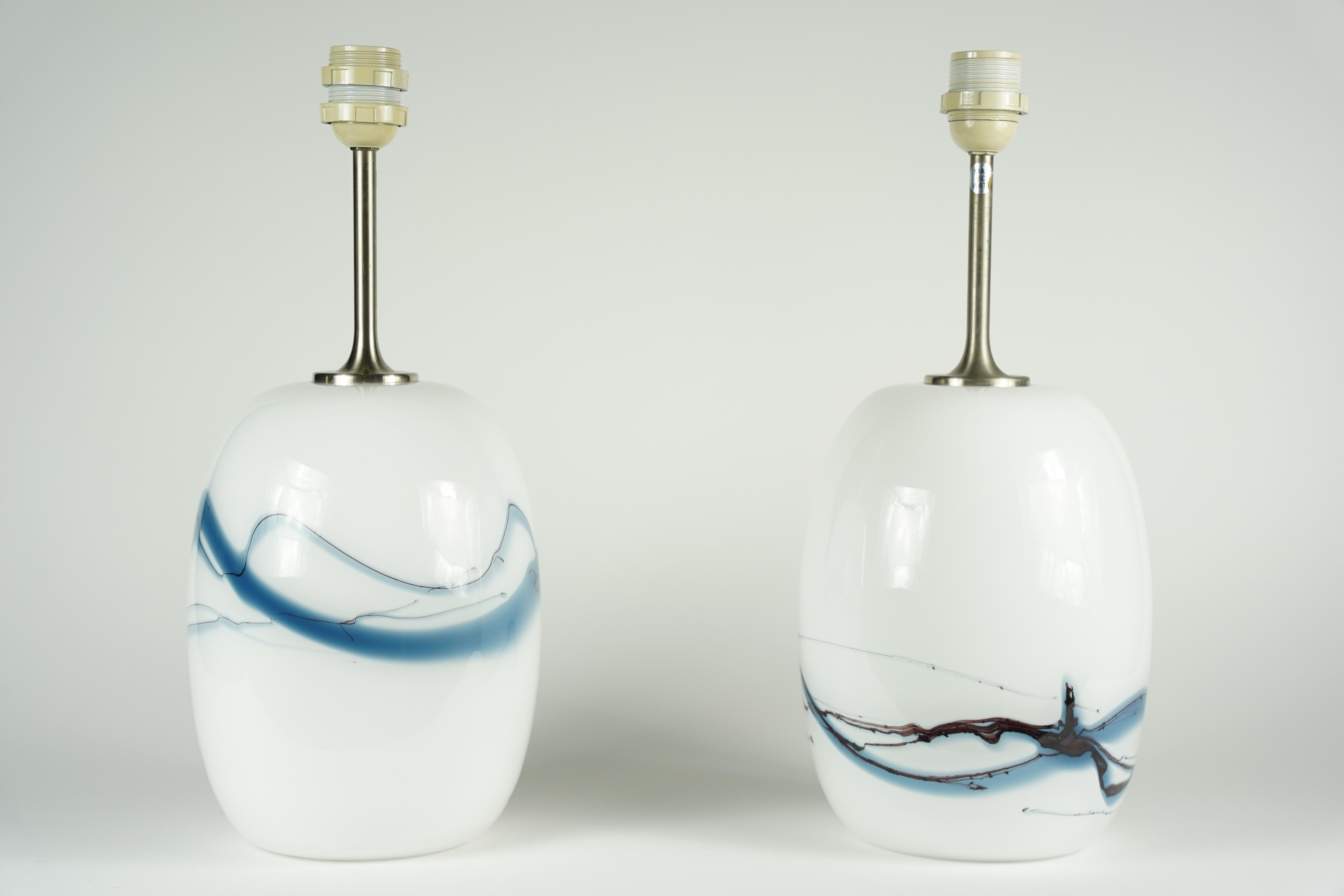 Zwei Holmegaard-Lampen mit gebürsteten Stahlbeschlägen von Holmegaard, Dänemark 1984. Weiße Glassockel mit einer Vielzahl von blauen und schwarzen Glasfarben, die unter dem glatten, klaren Glas schmelzen, entworfen von Michael Bang, 1984.
Die Höhe