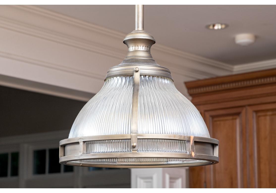 Pair of holophane glass pendant lights in antique bronze finish metal with stationary rods and ceiling plates.
The holophane glass shades are accentuated by a pierced and paneled frame that highlights the ribbing.

Dimensions: 13