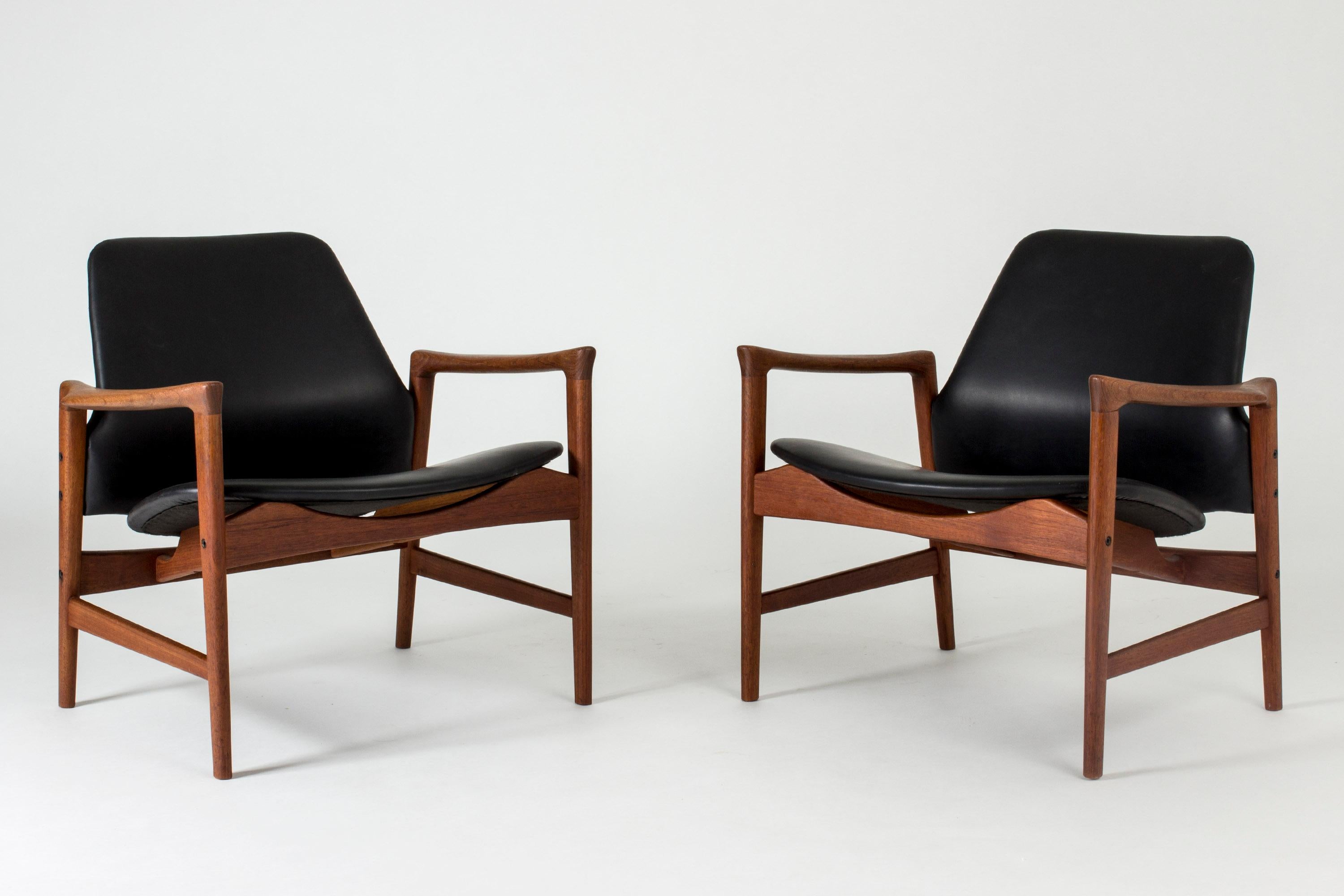 Pair of “Holte” lounge chairs by Ib Kofod Larsen. Made with teak frames, upholstered with black leather. Sculpted handles, cool silhouette. Great to sit in.