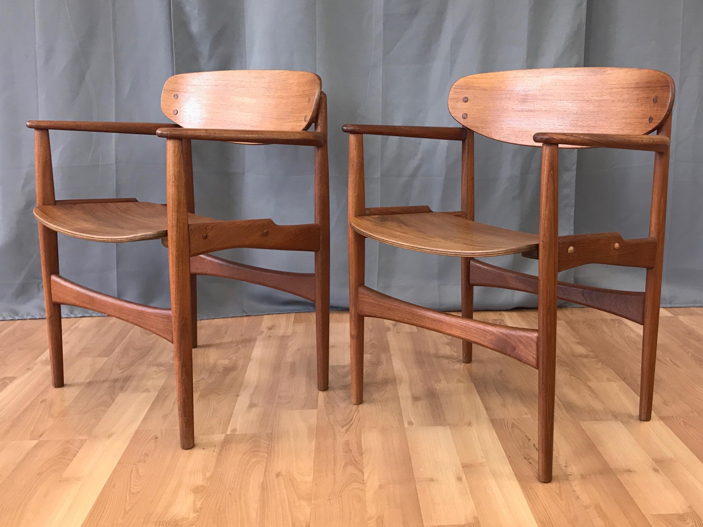 A pair of rare 1950s Danish teak armchairs by architect and designer Arne Hovmand-Olsen for Jutex.

Excellent craftsmanship and details on display throughout. Solid teak frame with sculpted arms, gunstock side stretchers, and tapered front and back