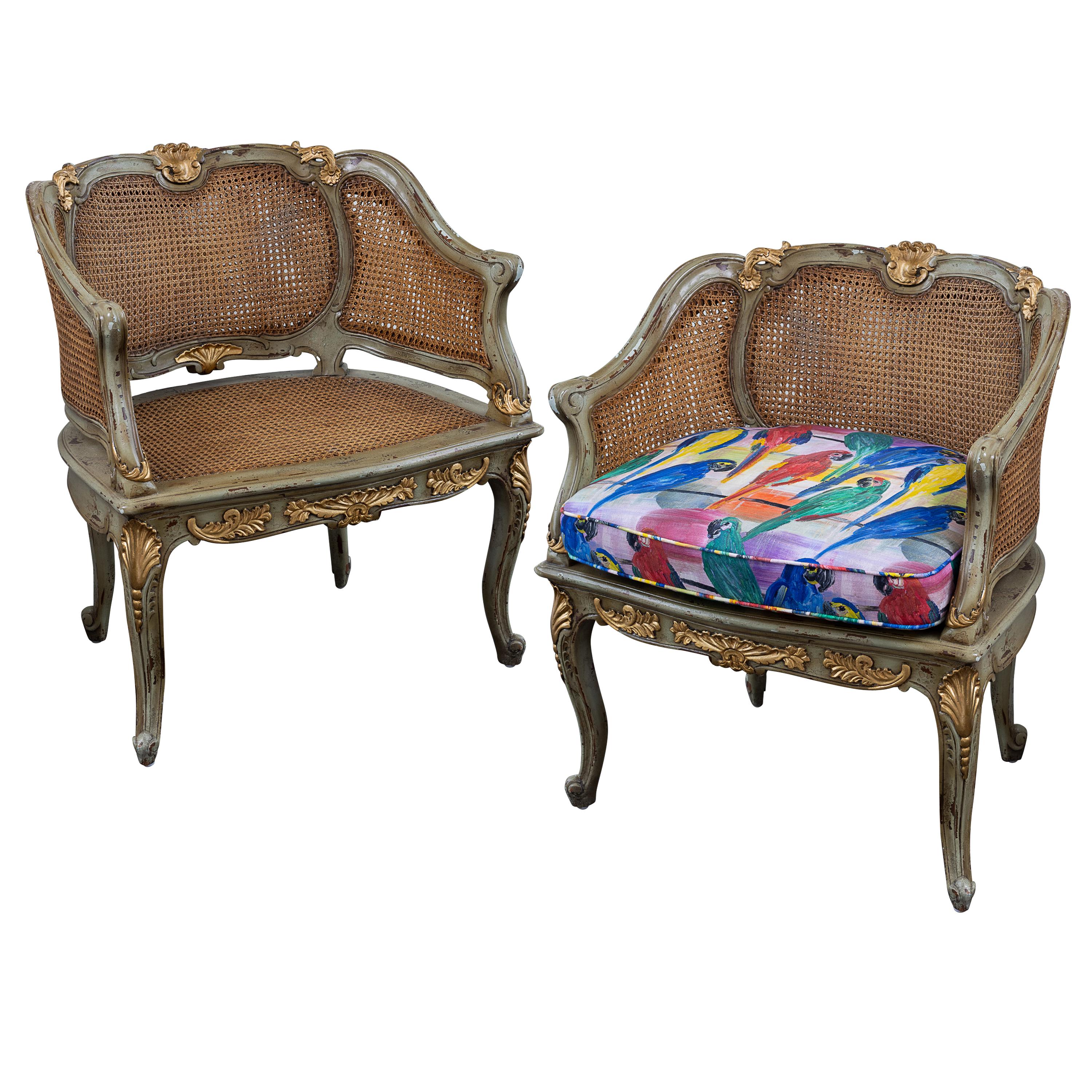 Paar französische Bergere-Stühle im Stil Louis XV aus dem frühen 19. Jahrhundert mit Rückenlehne und Sitzfläche aus Rohrgeflecht. Handbemaltes Holz mit Blattgoldschnitzereien. Sitzkissen in Hunt Slonems Hunt's Parrots Print. Die Stühle können