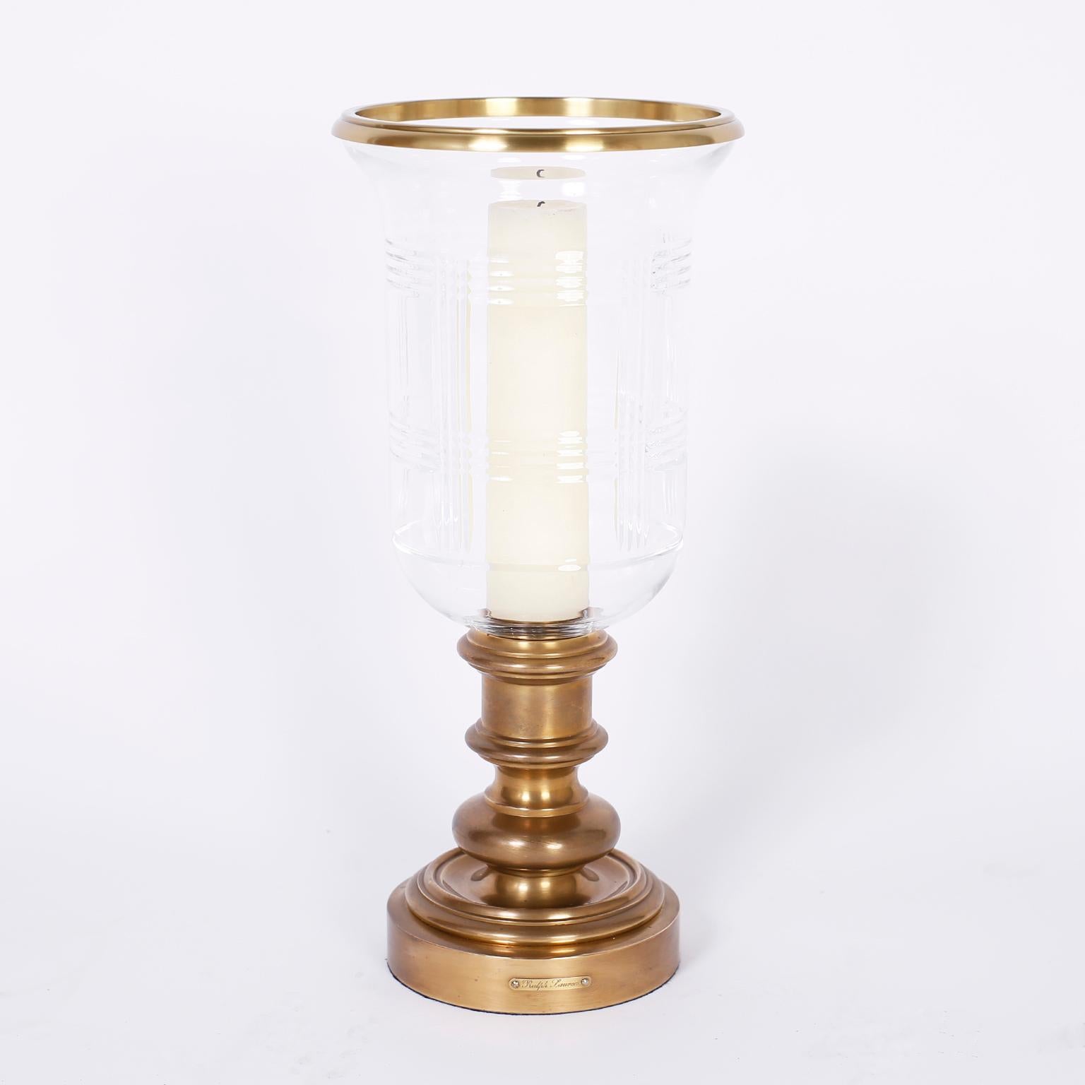 Pair of British Colonial hurricane candlesticks or holders with a brass ring circling the tops, glass shades with pressed geometric designs and burnished brass bases with Classic form. Signed Ralph Lauren on a plaque.