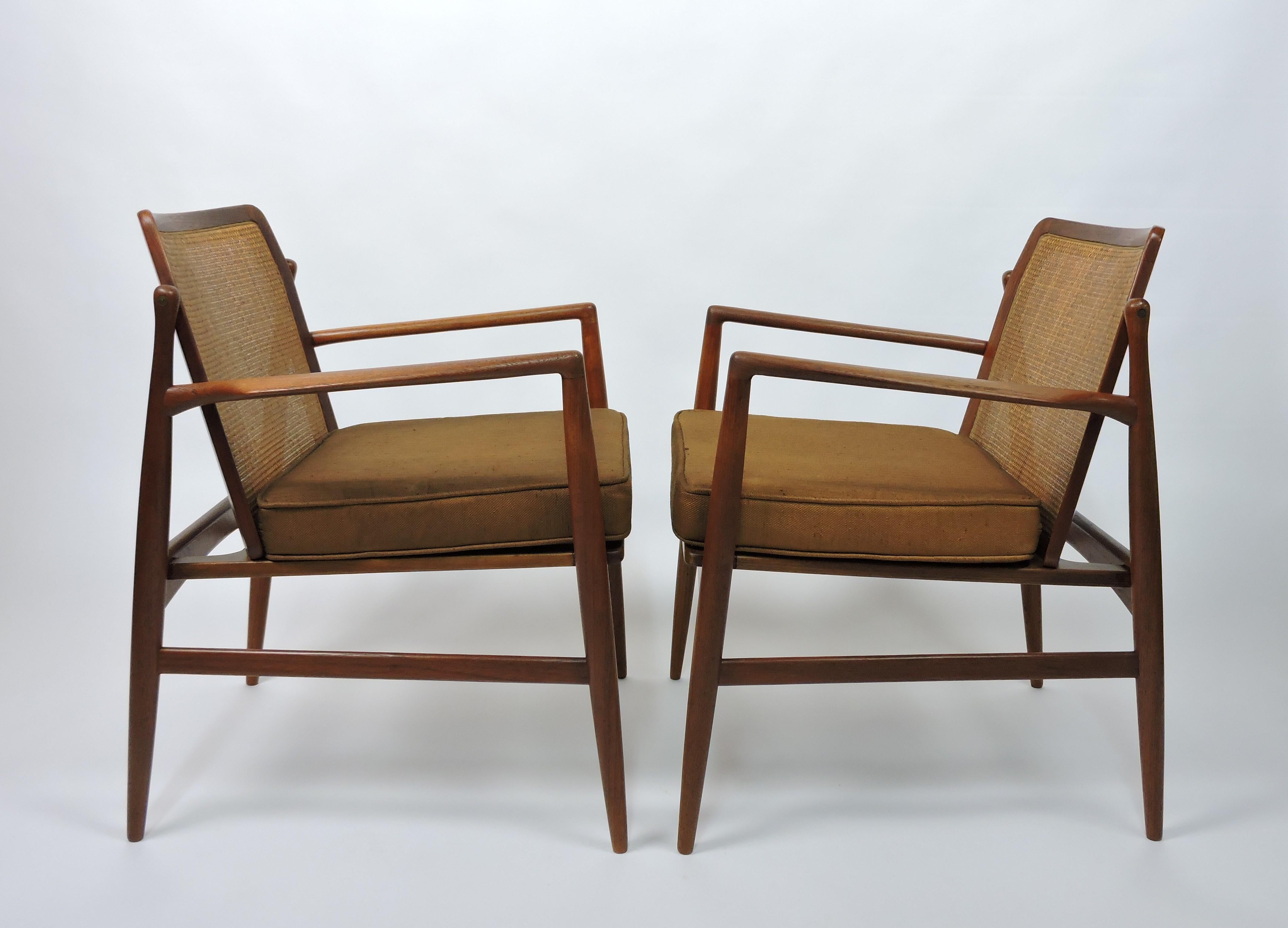 Eleganti e sofisticate sedie da salotto in teak disegnate da Ib Kofod-Larsen, prodotte in Danimarca e importate da Selig. Queste sedie hanno una bellissima struttura in teak scolpito, uno schienale in canna e sedute con cuscini sciolti. Etichettato